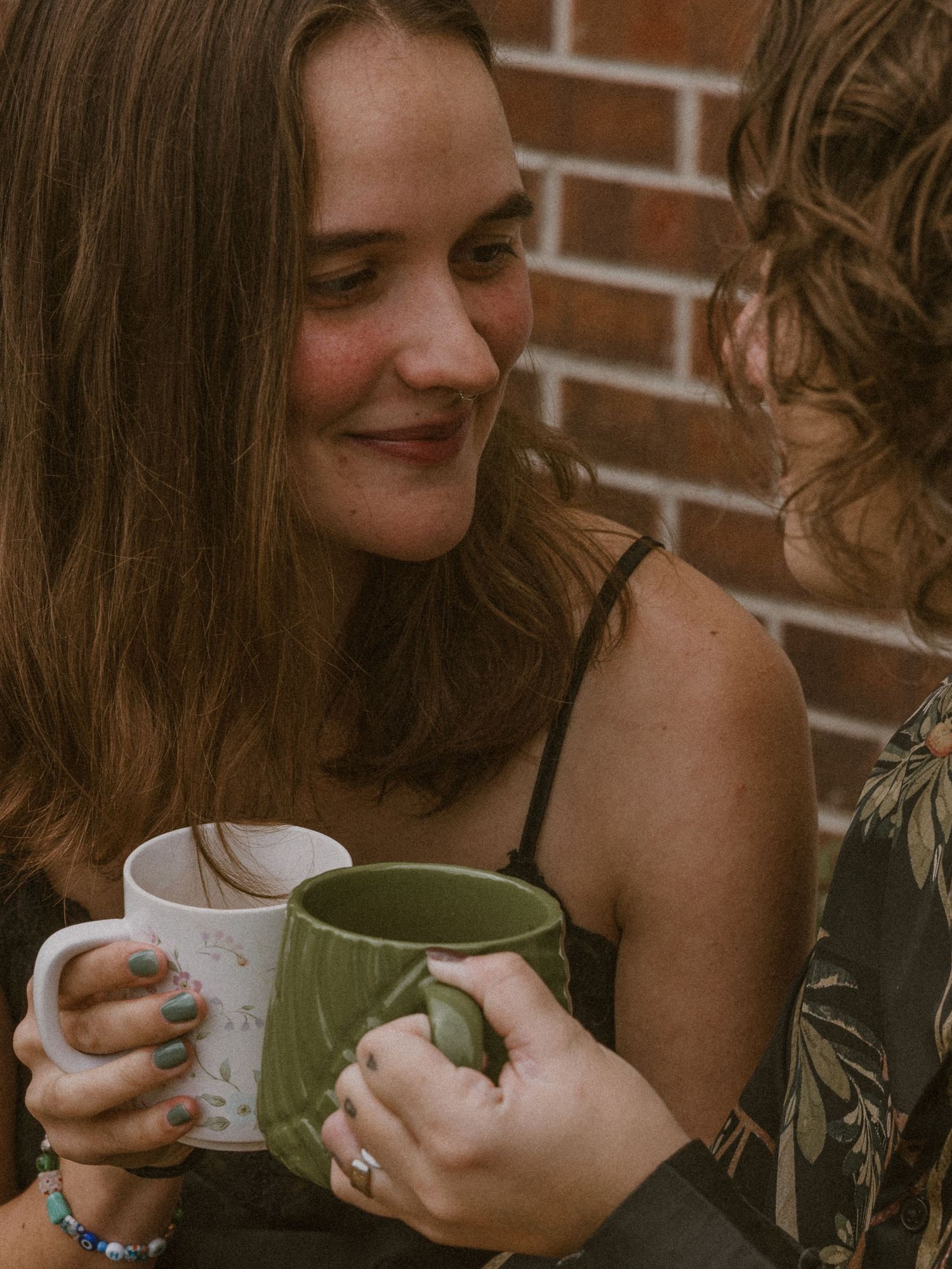 Two people holding coffee mugs while sharing an intimate moment near a brick wall.