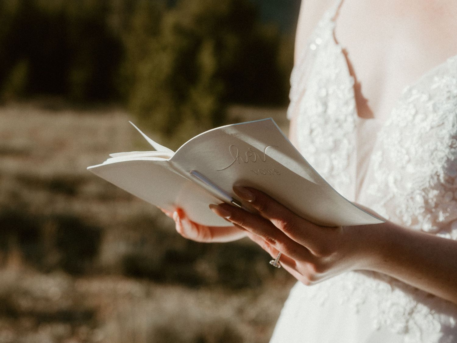 A close-up of hands holding handwritten vows during an outdoor wedding ceremony.