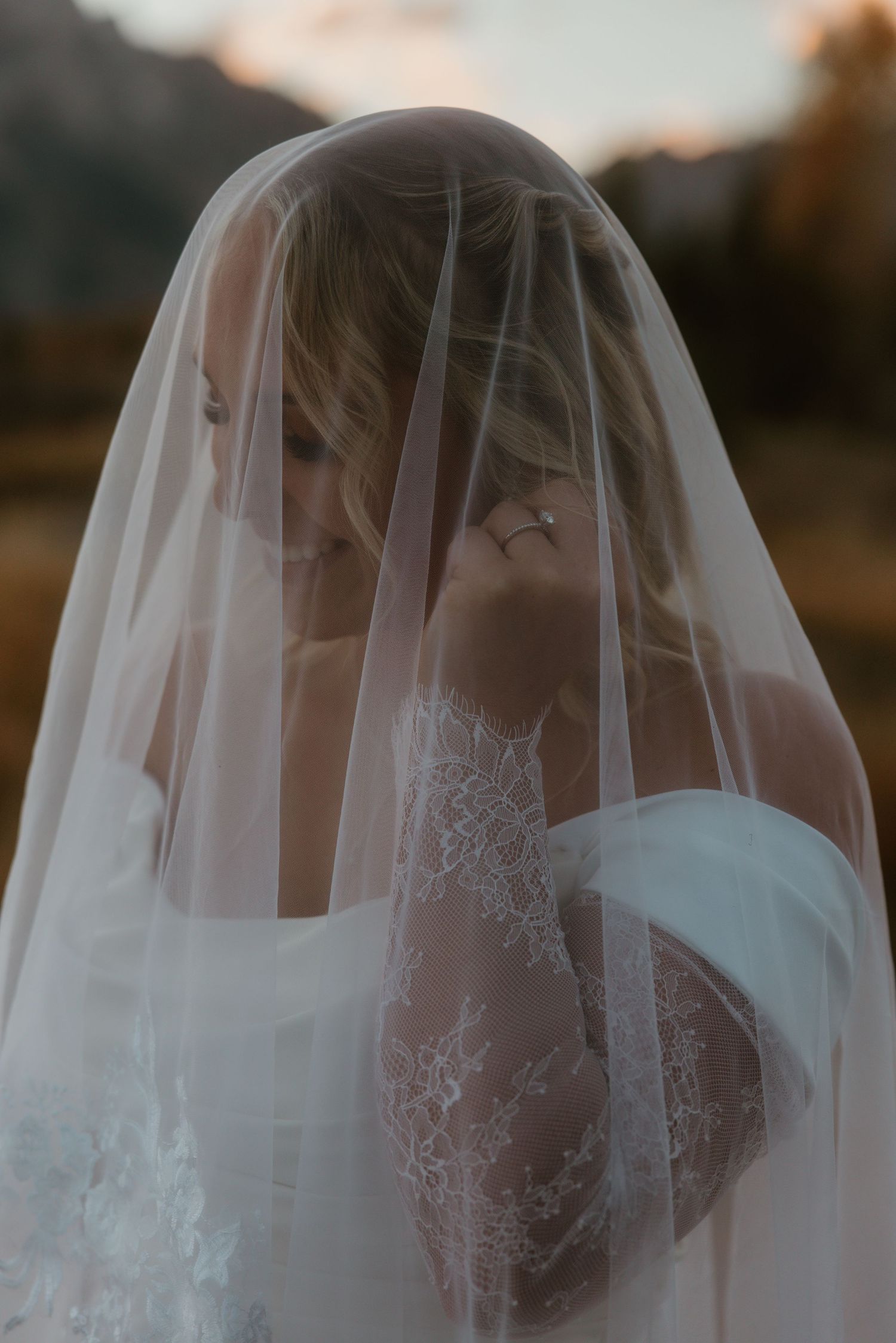 Artistic portrait through sheer veil of bride in lace wedding dress at sunset.