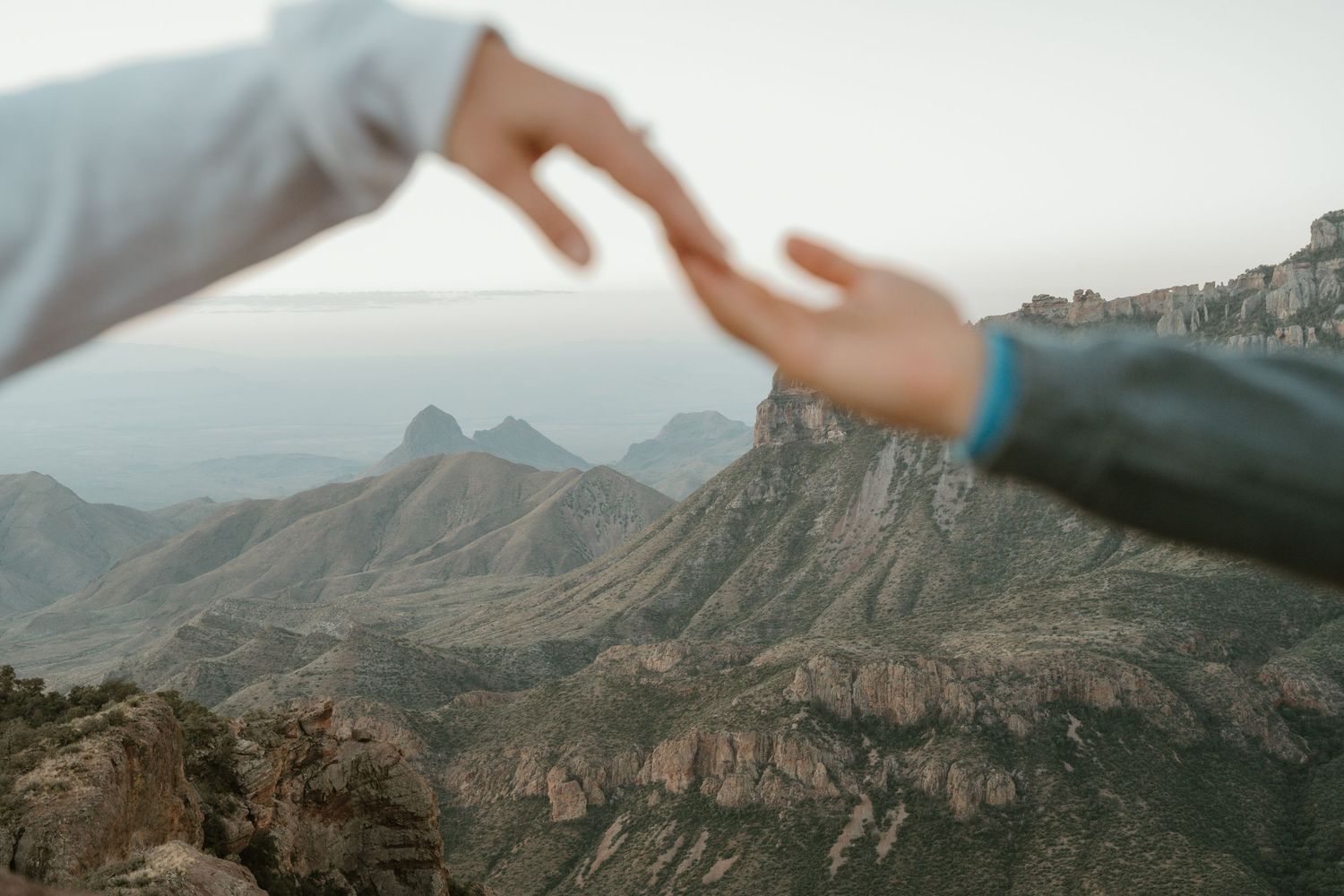 Reaching hands silhouetted against a dramatic mountain vista at sunset.