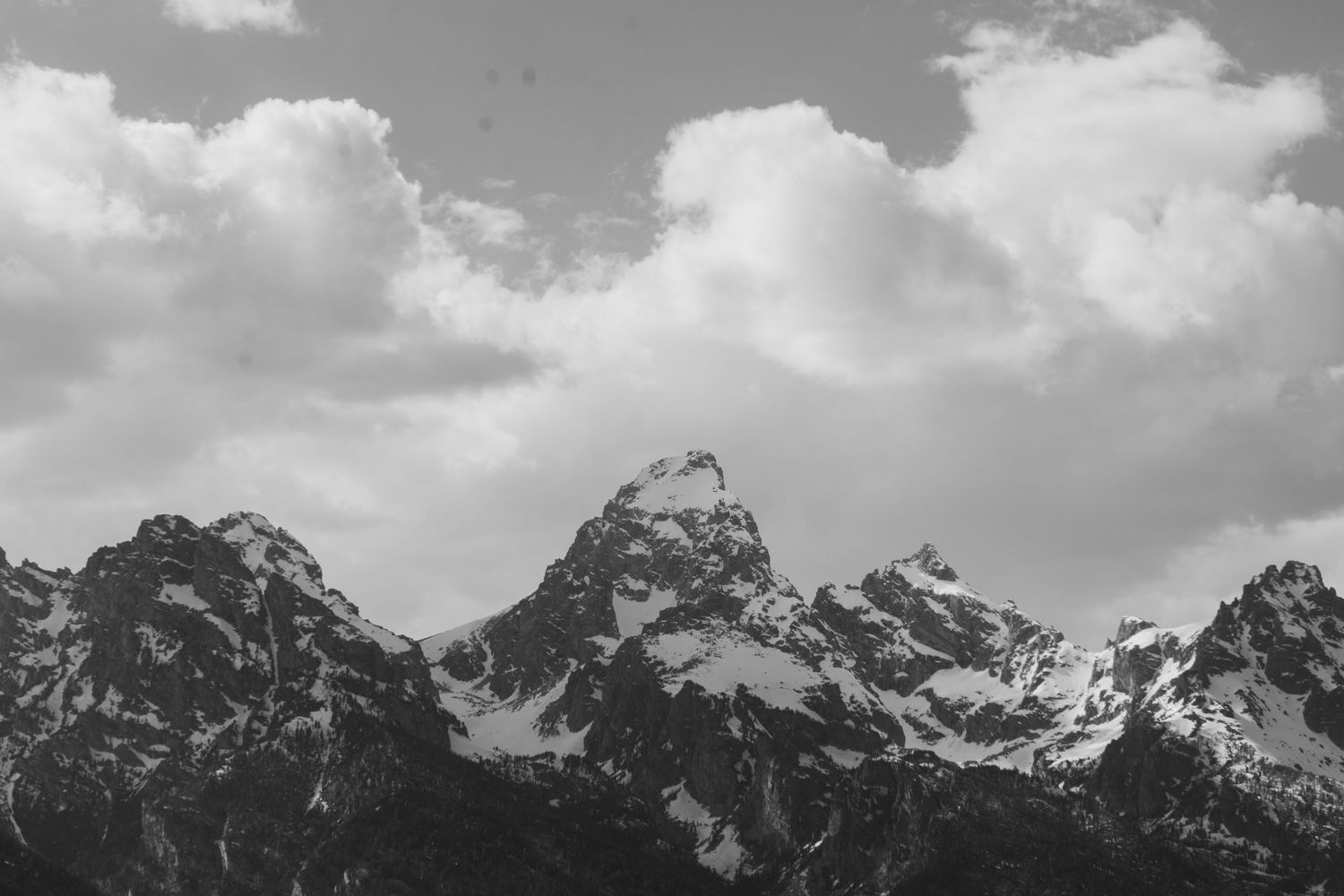 Black and white photo of snow-capped Grand Teton mountain peaks under dramatic cloudy sky.