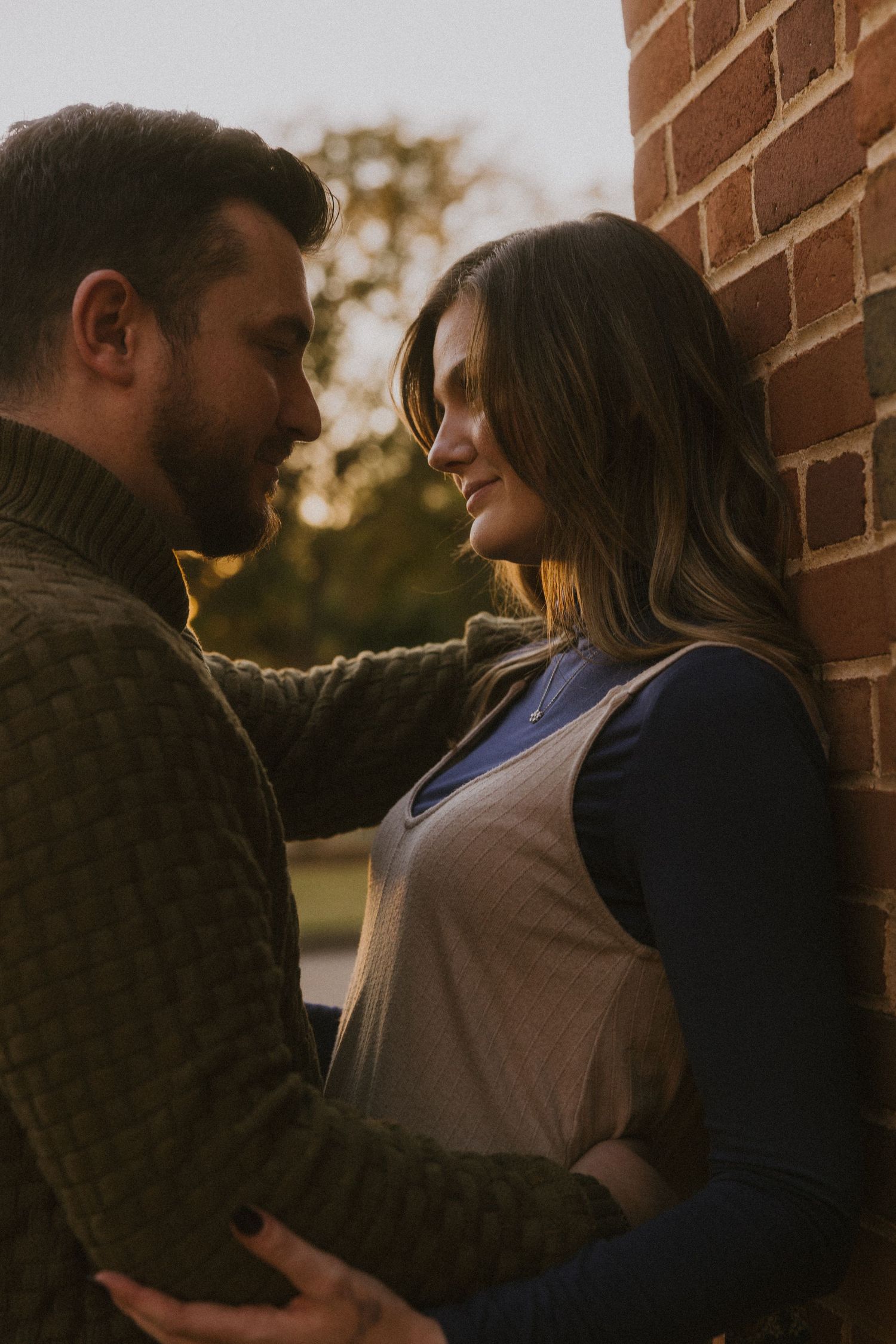 Romantic couple sharing an intimate moment against a brick wall at sunset.