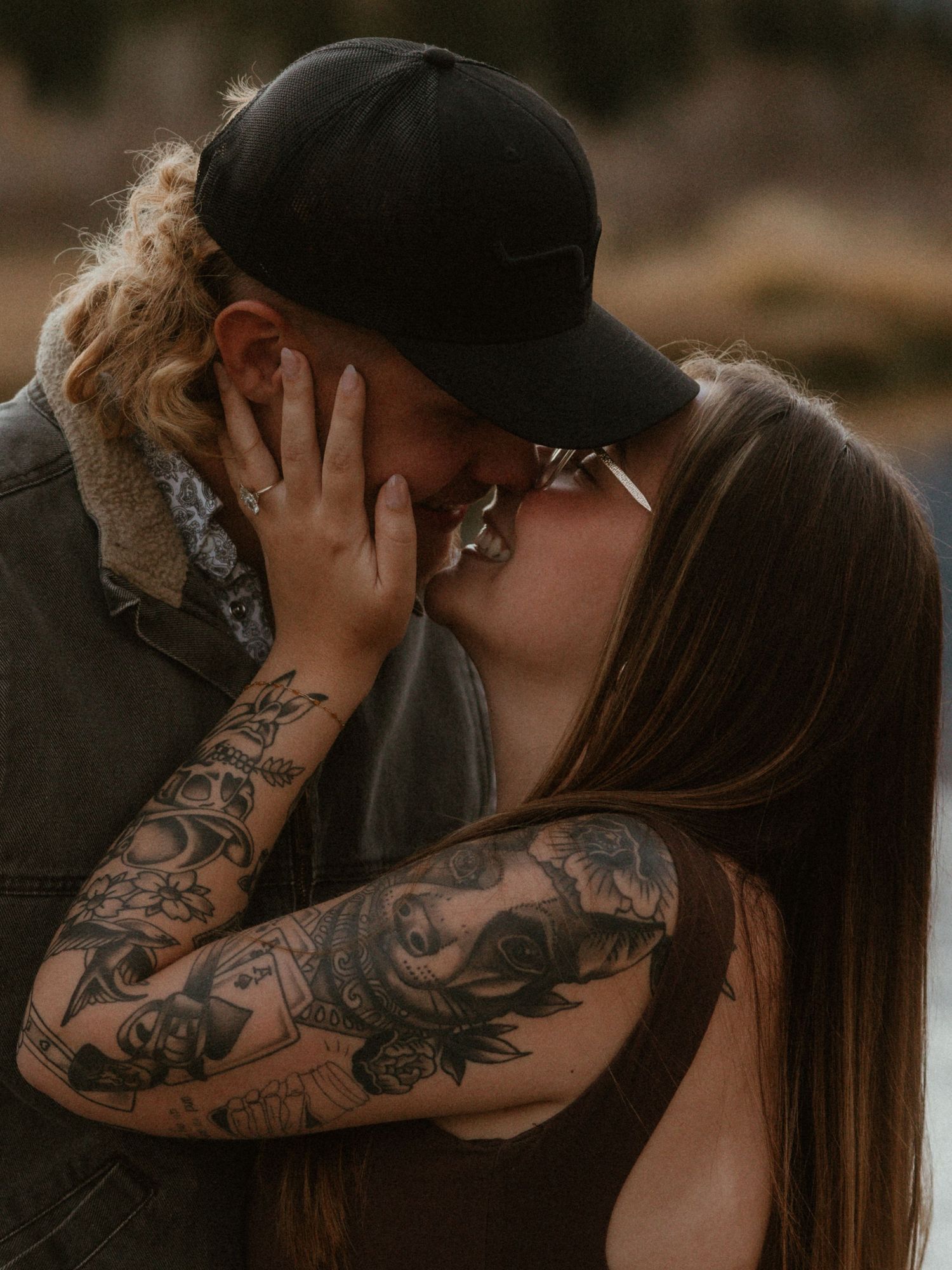 Close-up romantic moment captured against a moody dark background with visible tattoo artwork.