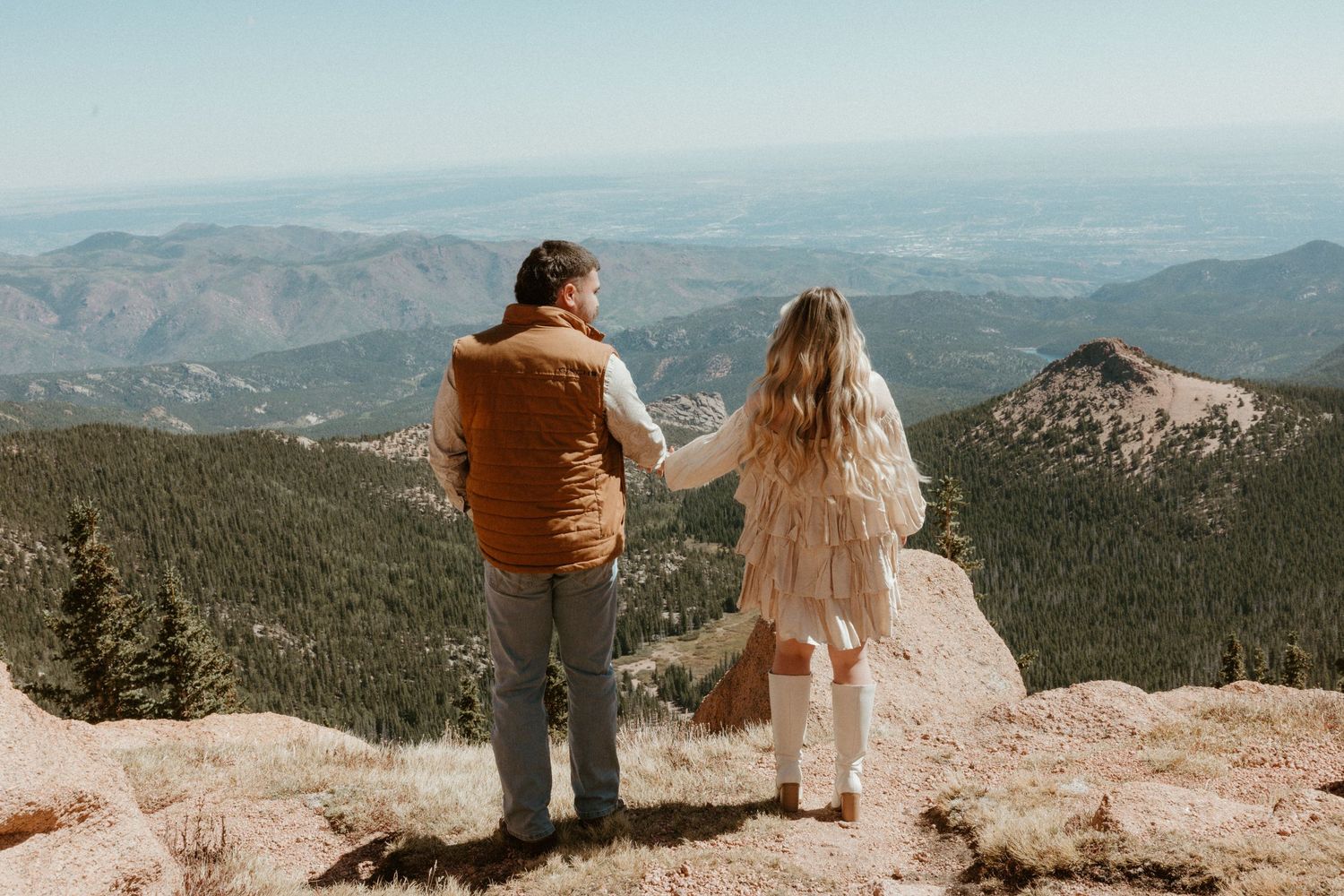 Couple enjoys scenic mountain vista while standing on rocky overlook surrounded by forest.