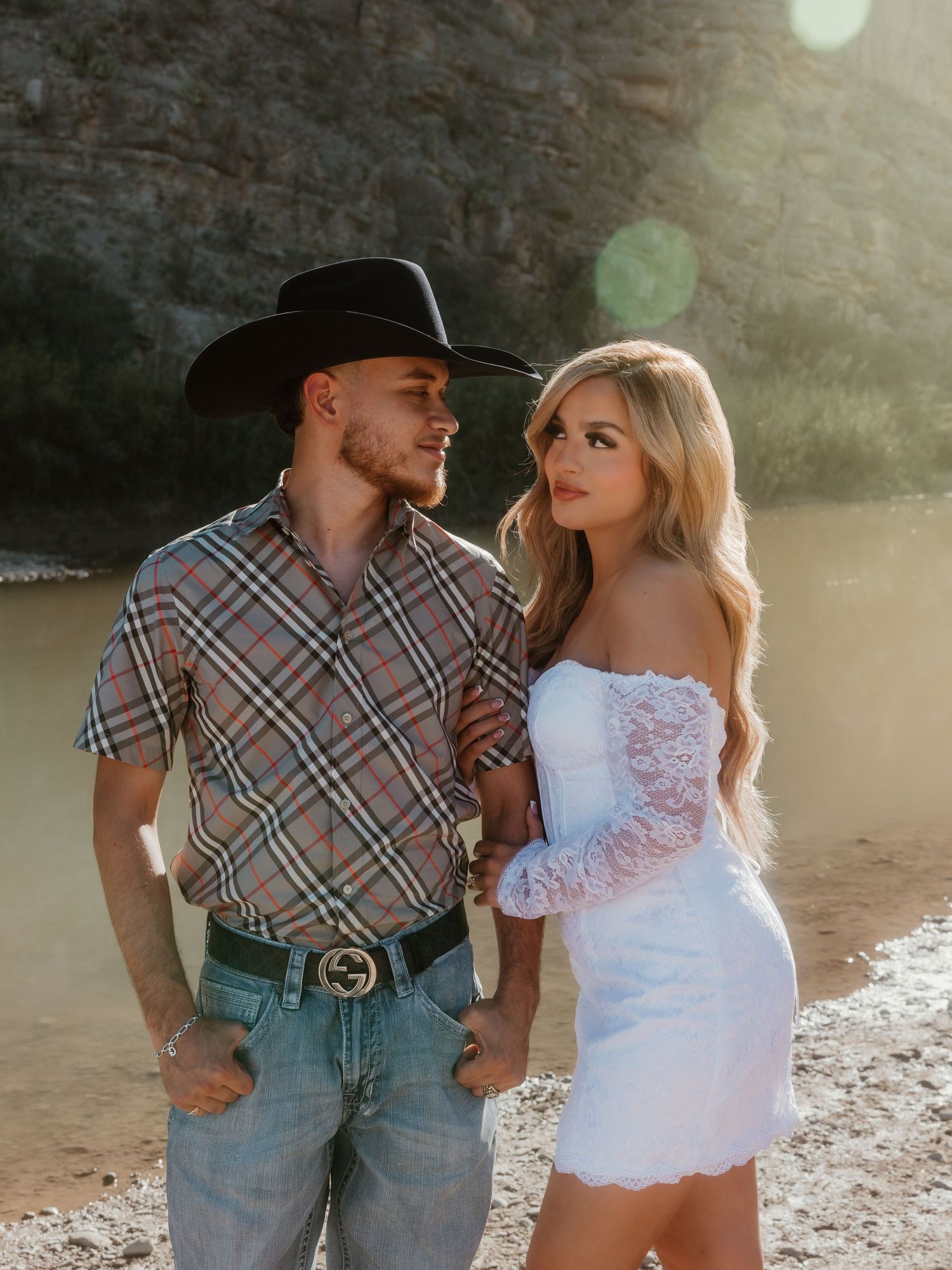 A romantic moment between a cowboy and woman in white dress against a scenic canyon backdrop.