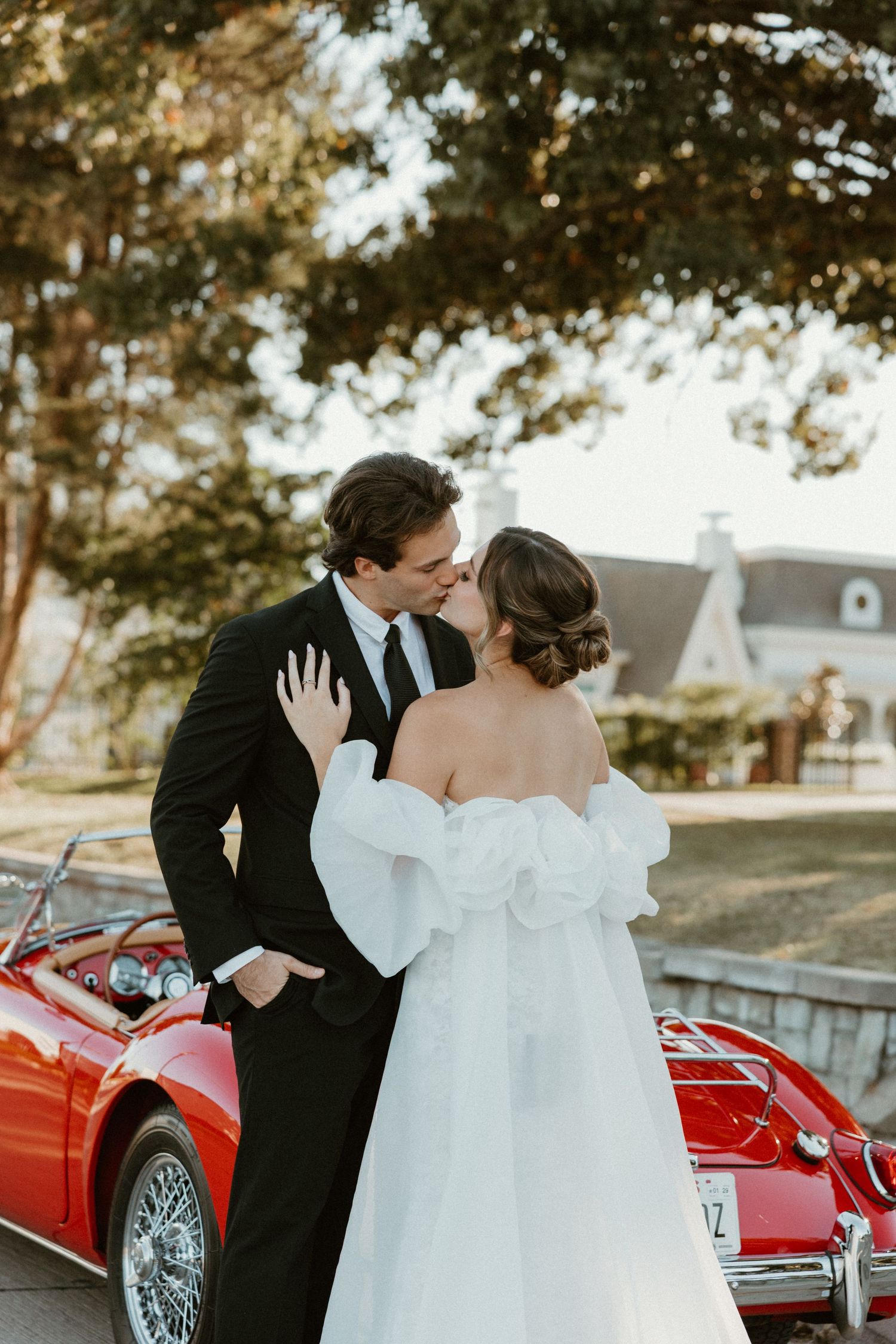 A classic red vintage car serves as an elegant backdrop for a wedding photo session.