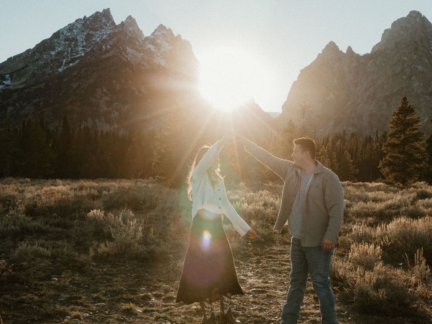 Sunlight streams through mountain peaks as a couple stands in a scenic wilderness setting.