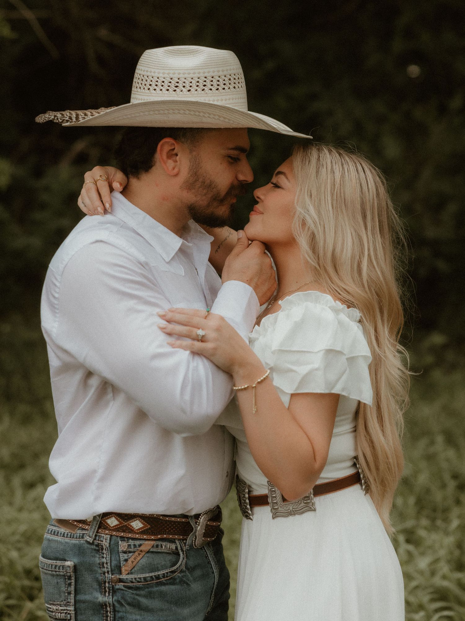 A romantic couple in western attire sharing an intimate moment outdoors against a natural backdrop.