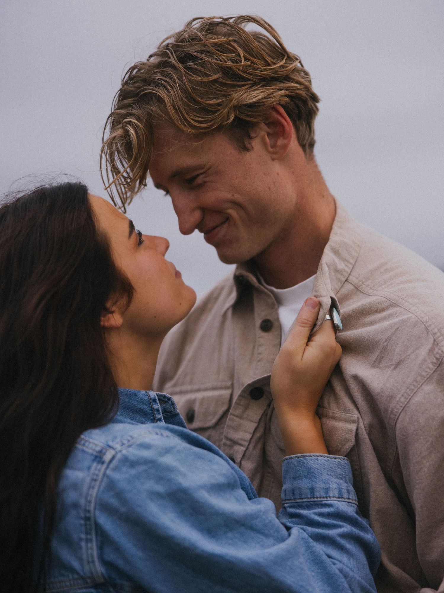 An intimate close-up moment between two people wearing denim and beige clothing.