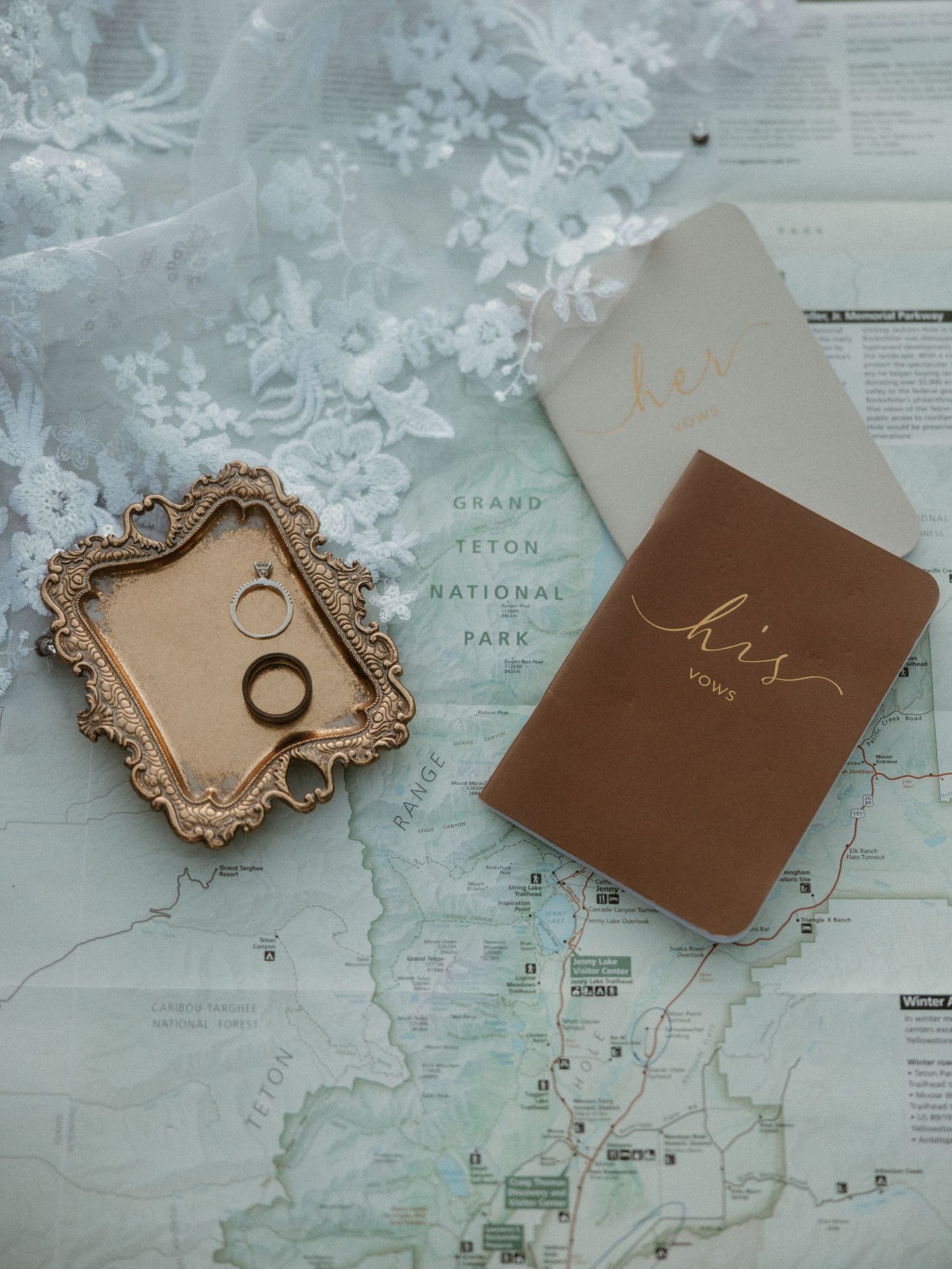 Wedding rings on ornate tray with vow books and Grand Teton National Park map.