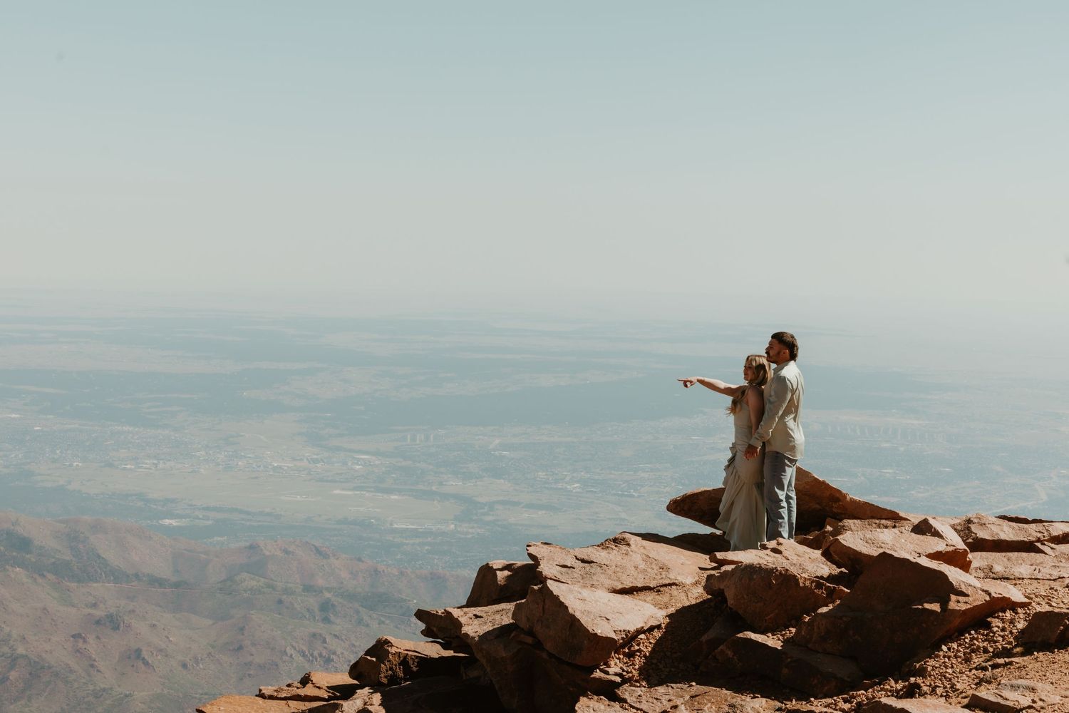 Figure stands triumphantly on mountain peak with arms spread wide against misty mountain backdrop.