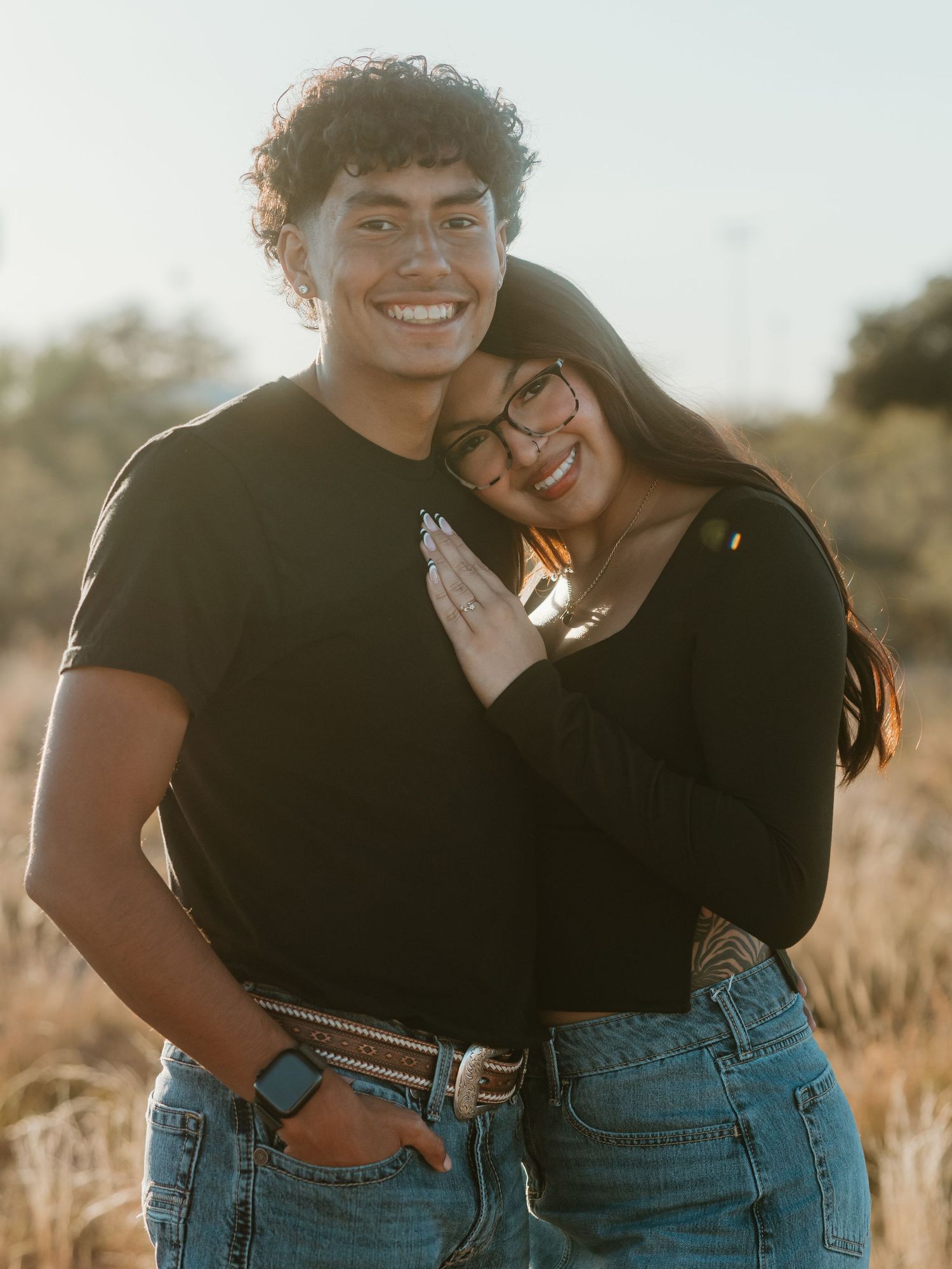 Couple in casual denim and black outfits sharing joyful moment in warm sunlight.