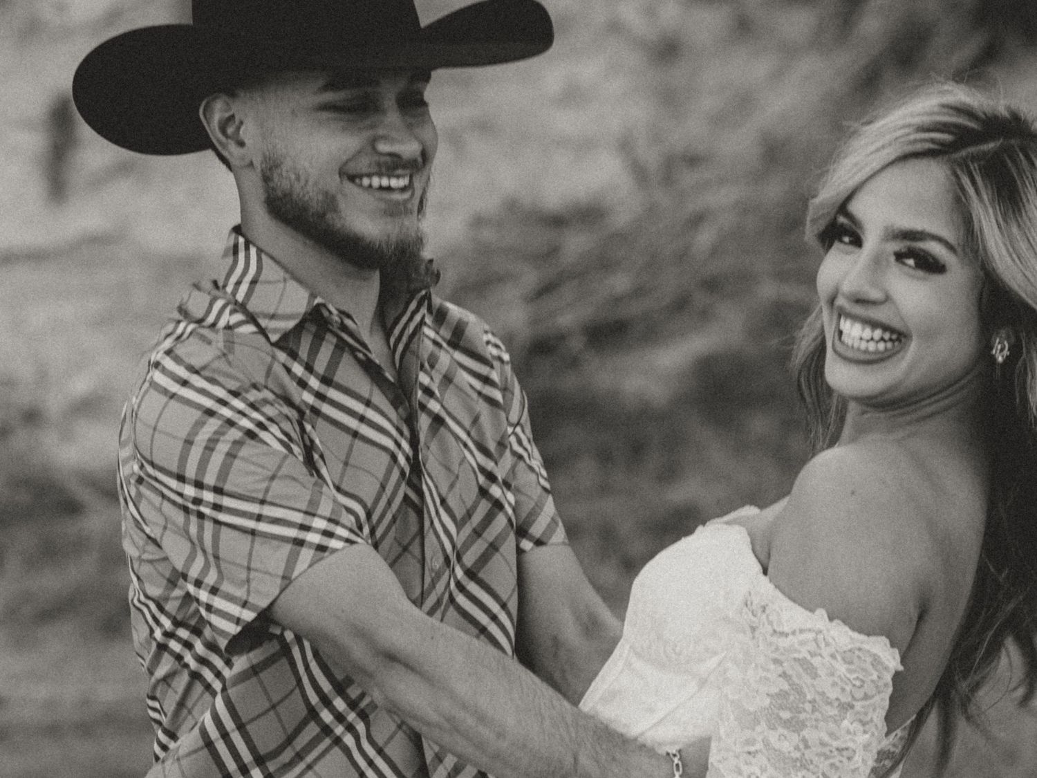 A romantic couple shares a joyful moment together in western attire against a bright background.