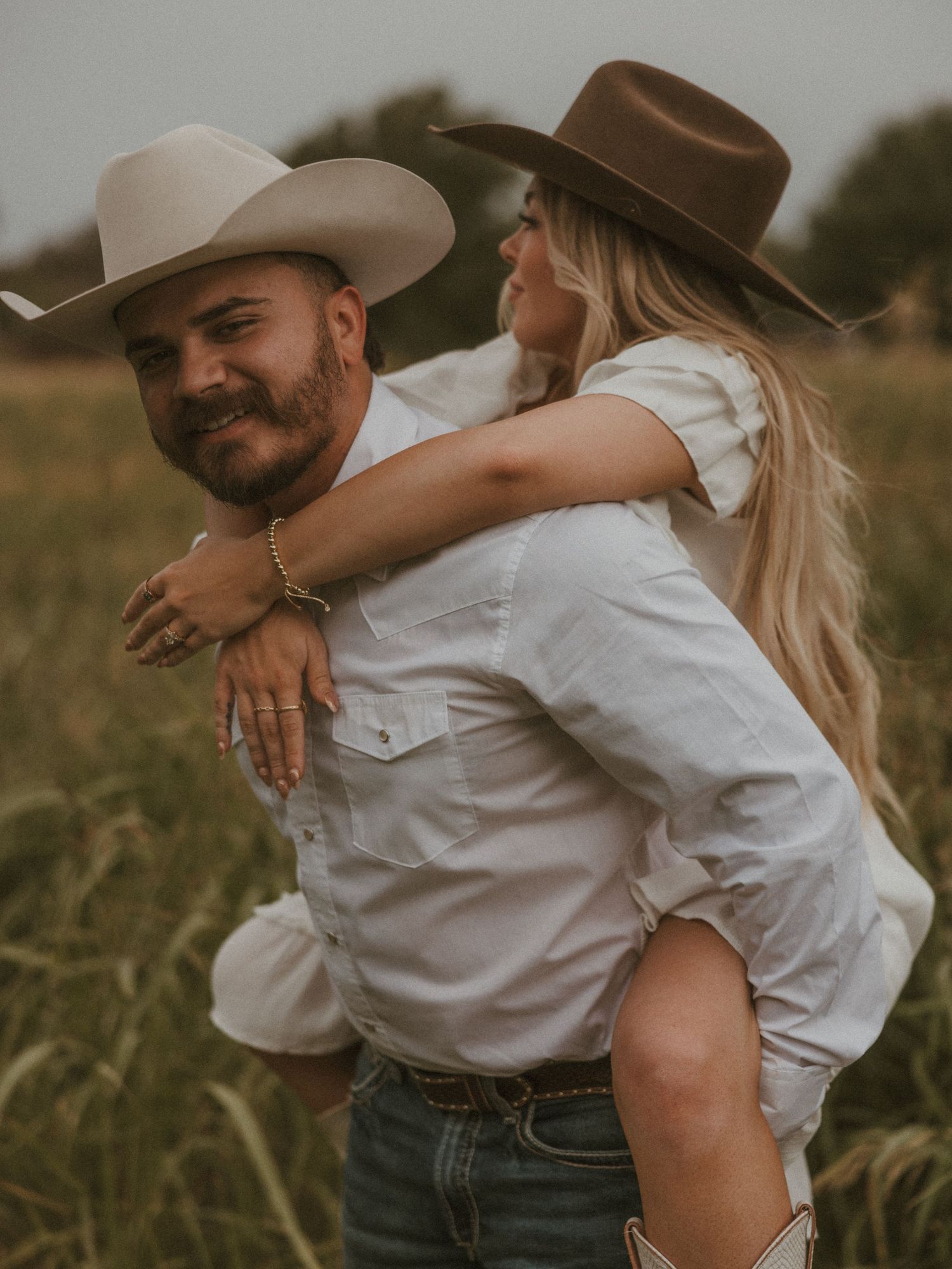 Couple in matching white outfits and cowboy hats embracing outdoors.