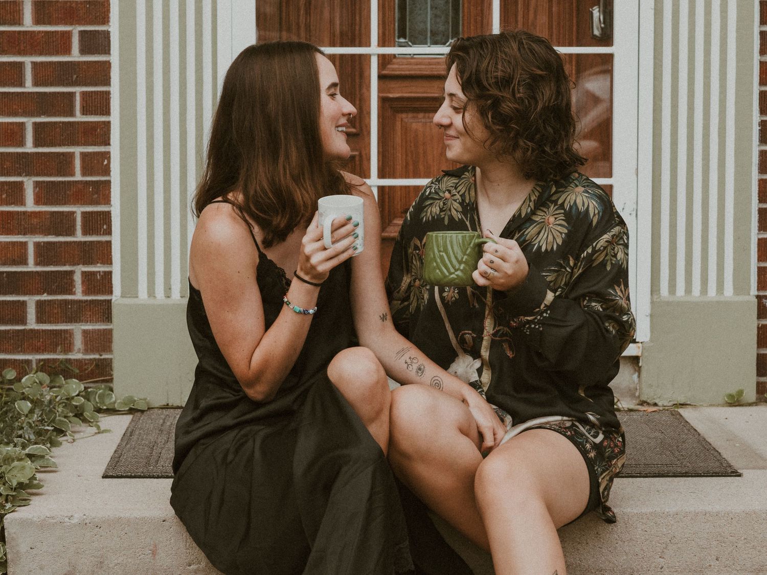 Two people sitting and talking on outdoor steps with brick building backdrop.