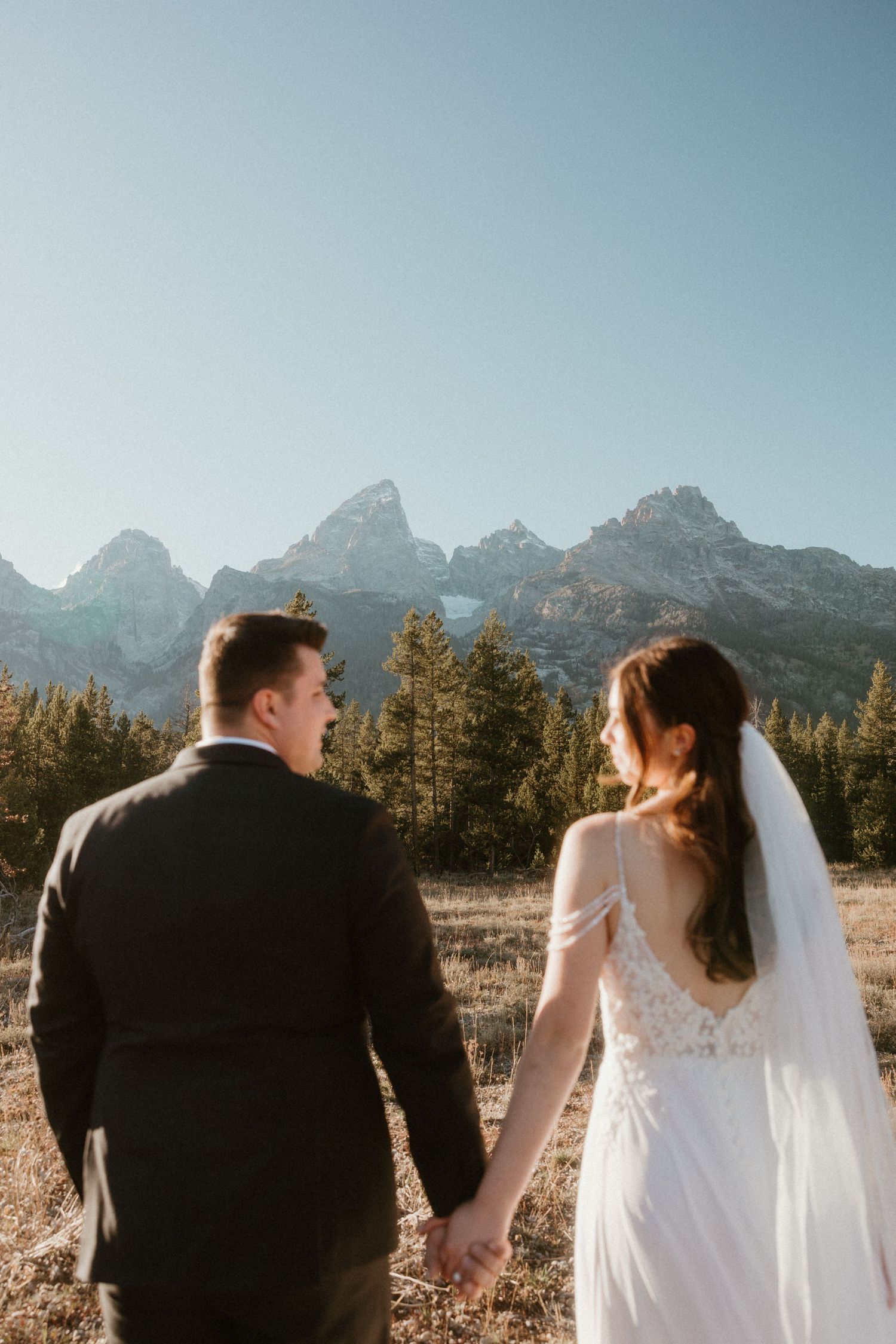 A newlywed couple stands together against a backdrop of majestic mountain peaks.