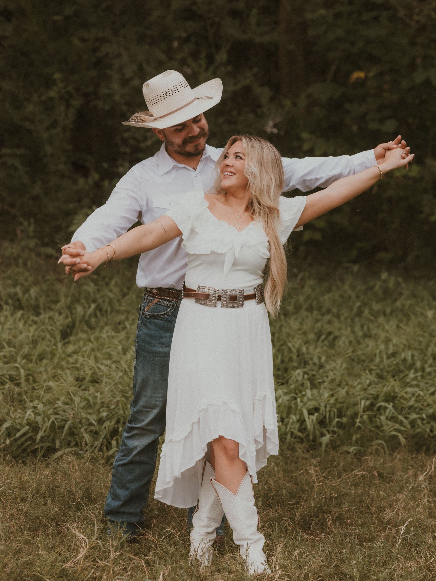 Couple in western-inspired outfits dancing freely in a wild grass field.