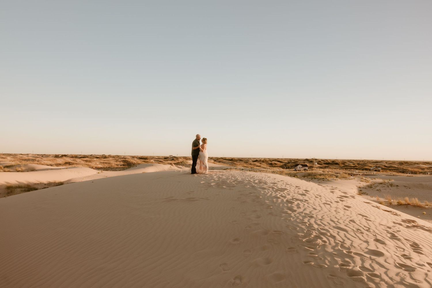 A distant view of newlyweds standing on a sand dune during their desert wedding.