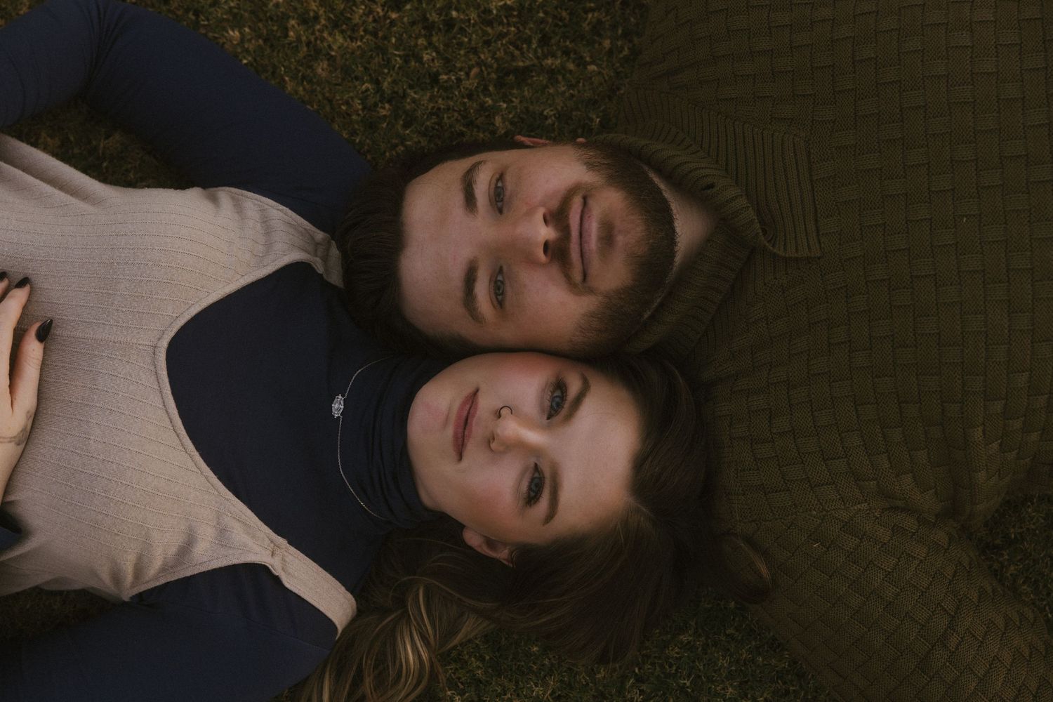 Couple lying together on grass sharing a playful moment.