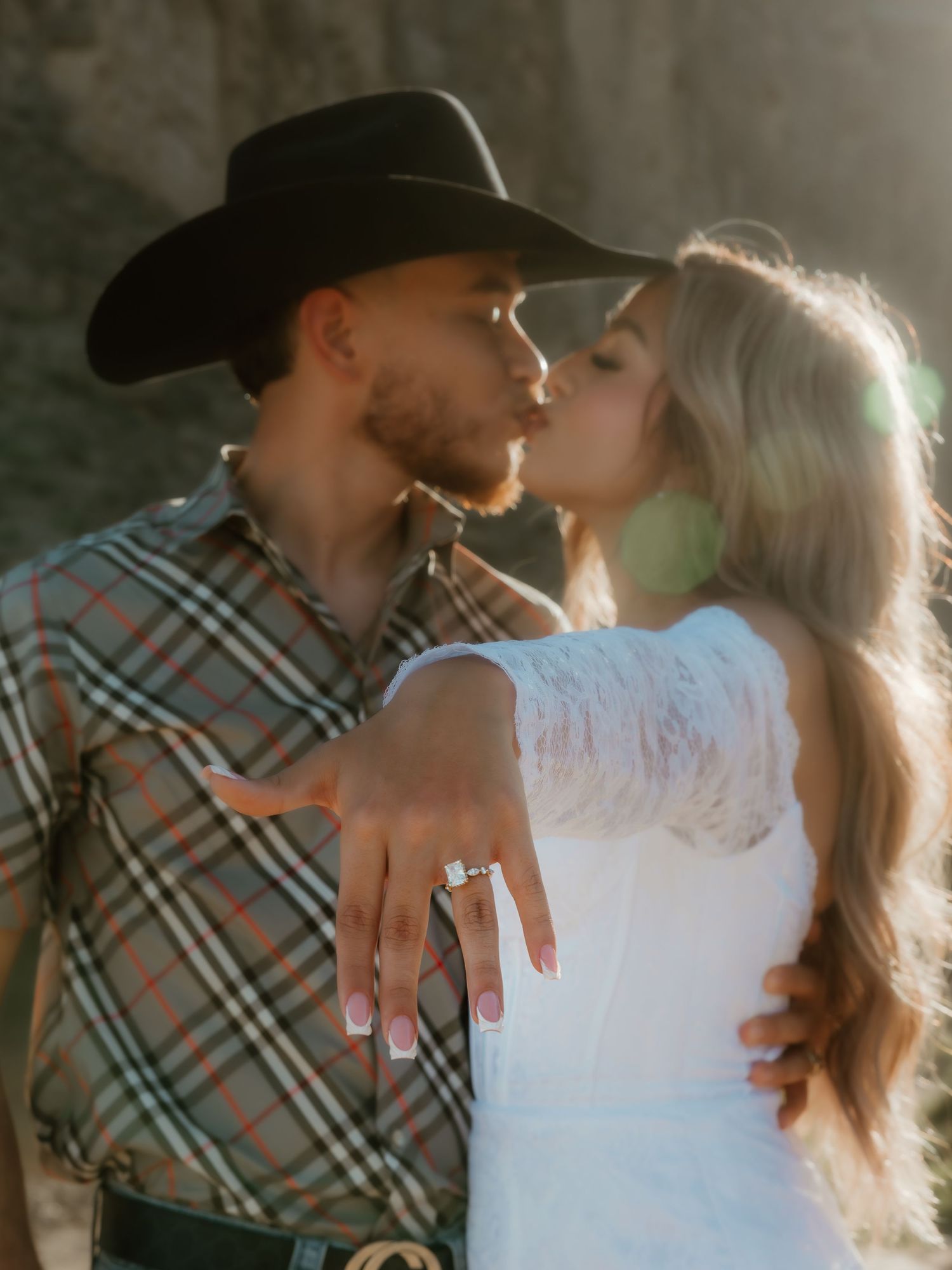 A couple in western wear embraces closely, with the woman's engagement ring visible.