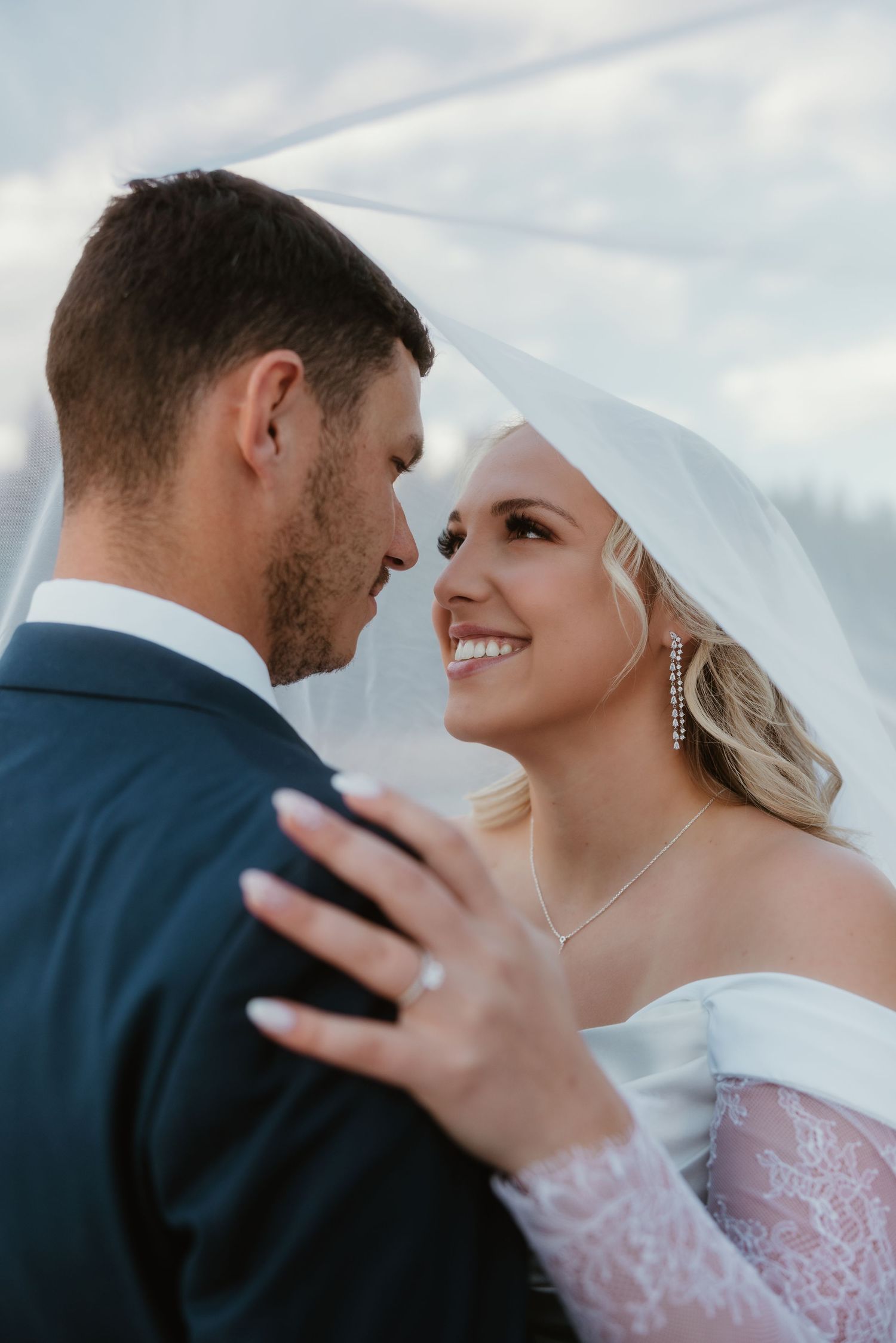 Romantic wedding portrait of couple embracing with bride wearing lace gown and flowing veil.