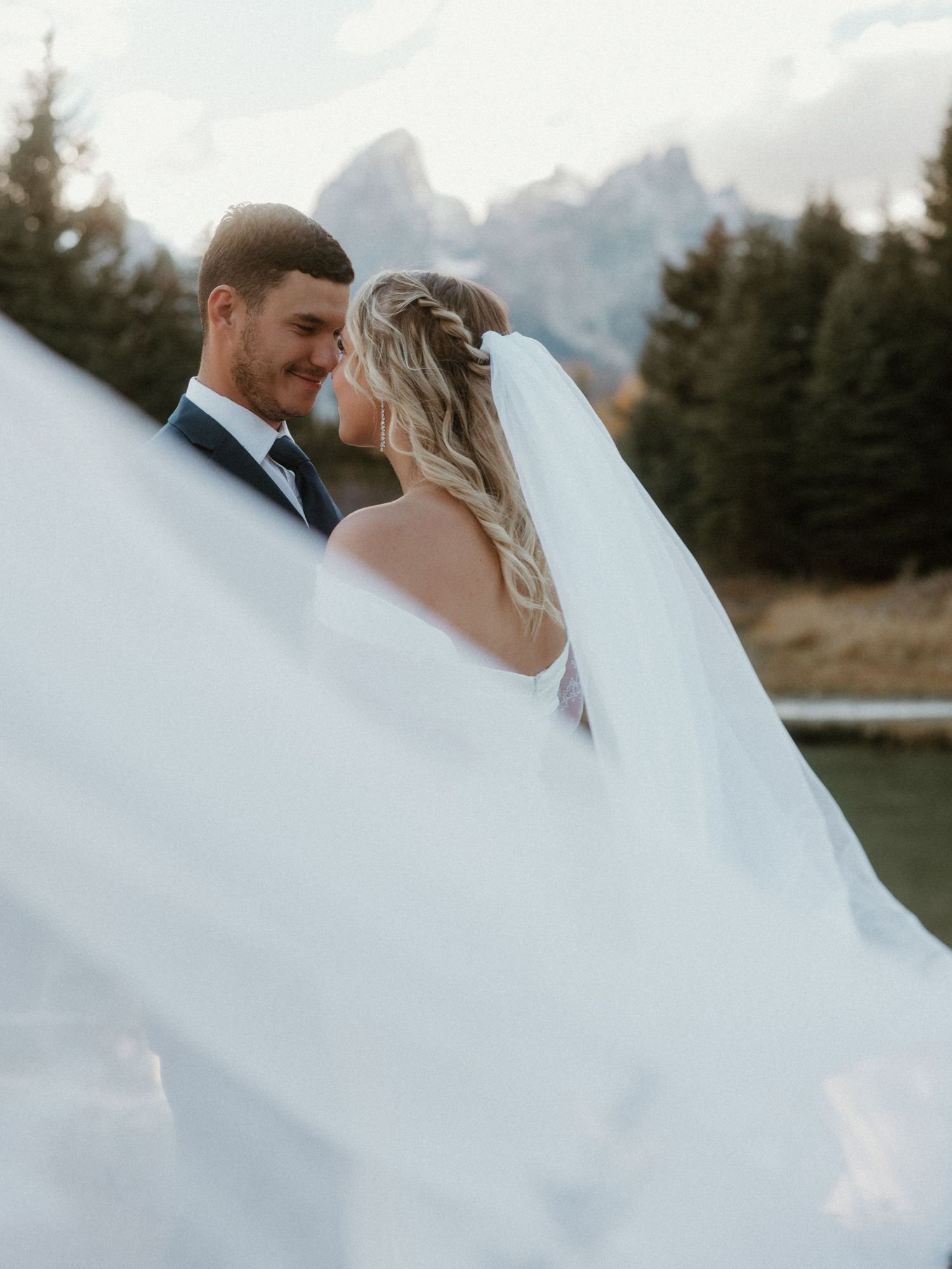 A romantic wedding photo with a flowing veil against a mountain backdrop in golden light.