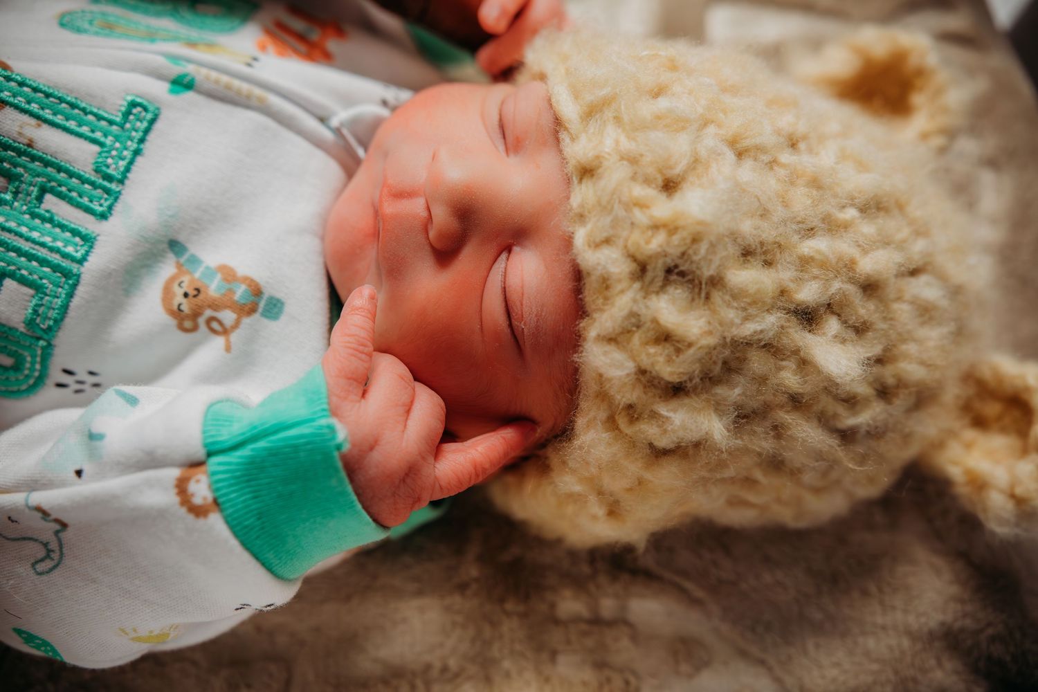 Sleeping baby wearing green and white outfit with soft plush toy nearby.