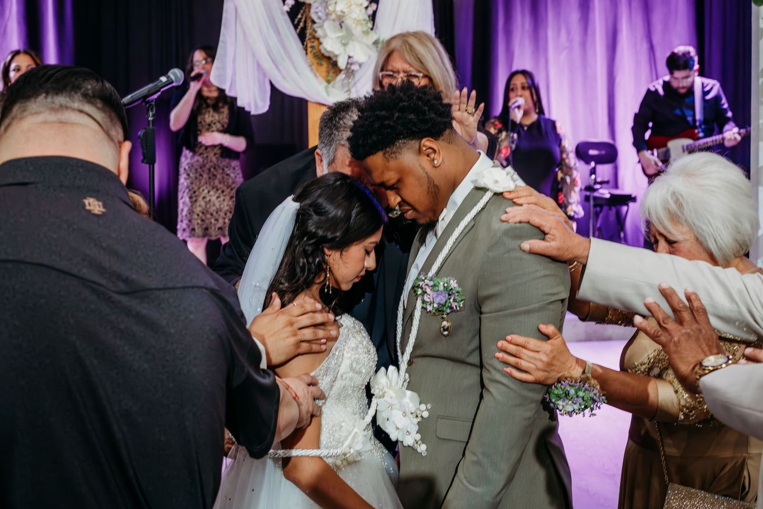 Wedding reception celebration with guests and newlyweds dancing under purple lighting in an elegant ballroom setting.