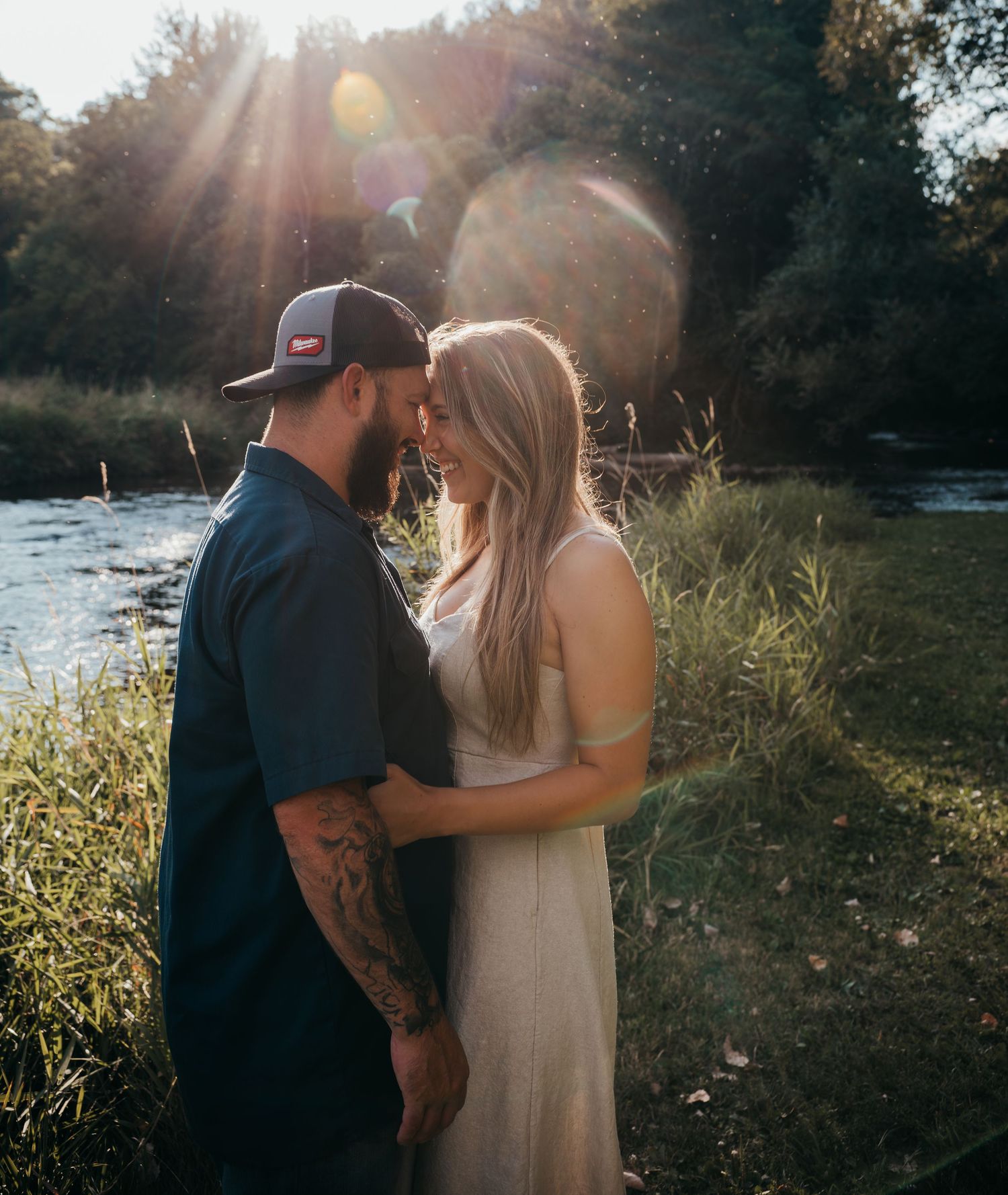 A romantic sunset photoshoot by a lake with tall grass and golden sunlight streaming through the trees.
