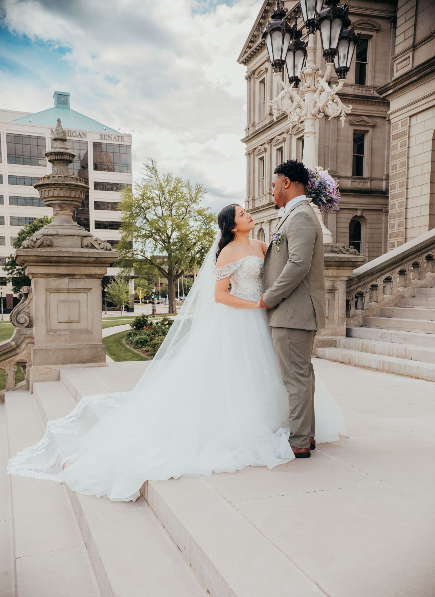 A couple in wedding attire share romantic moments on the grand stone steps of a historic building.