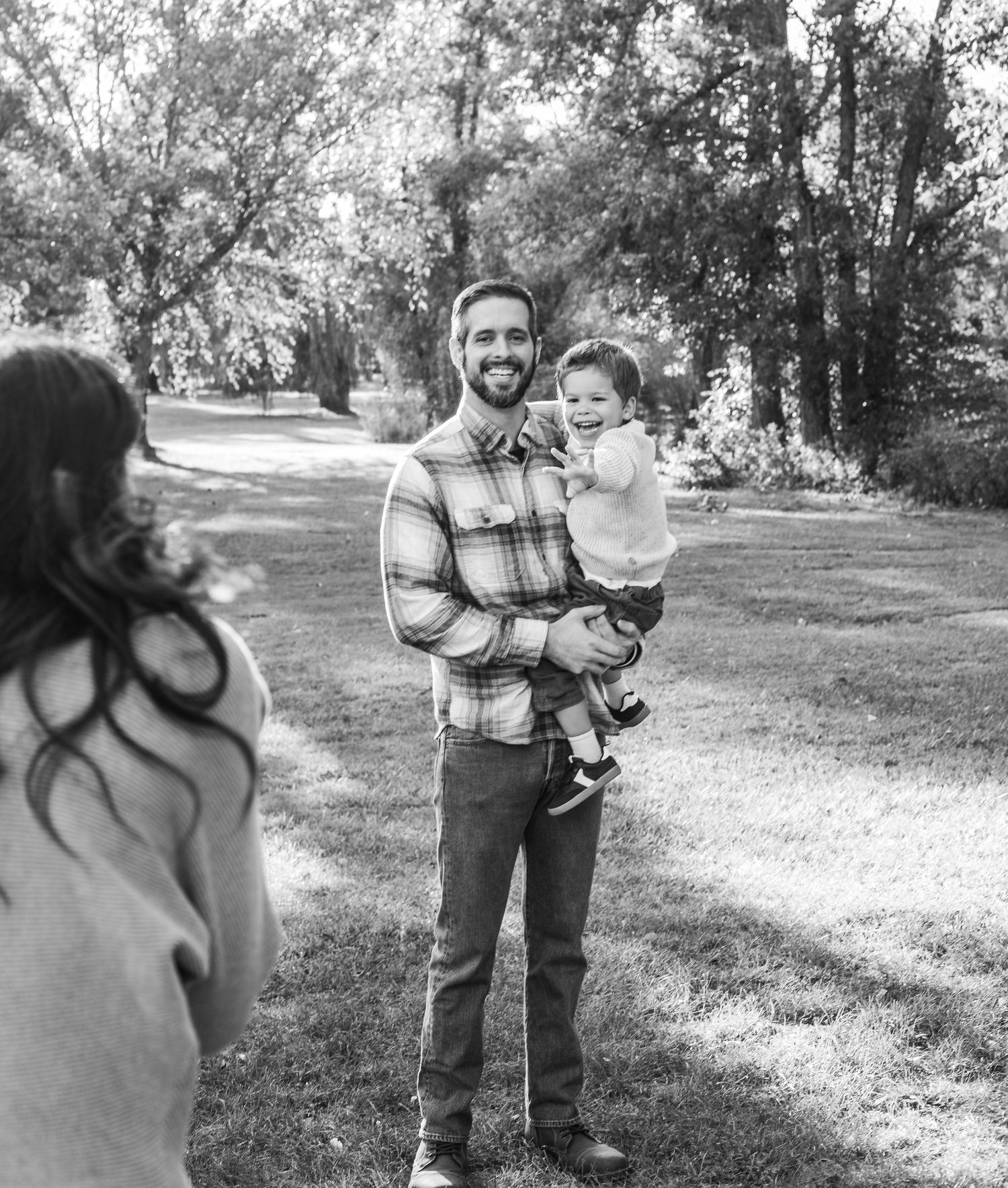 A sequence of black and white photos showing a person holding and interacting with a small child outdoors in a park setting.