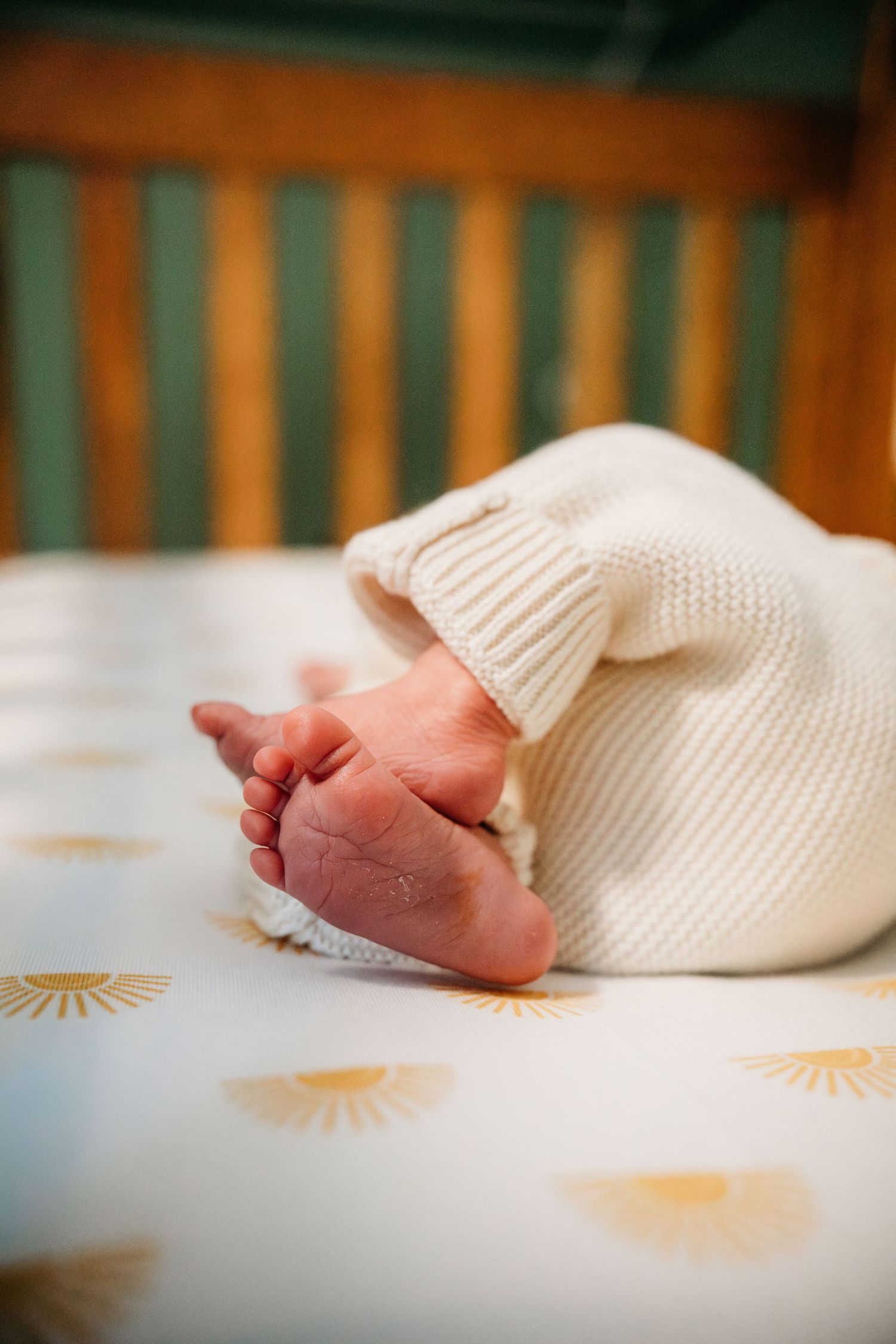 A series of close-up photos showing tiny baby feet against a white knitted blanket with orange sun patterns.