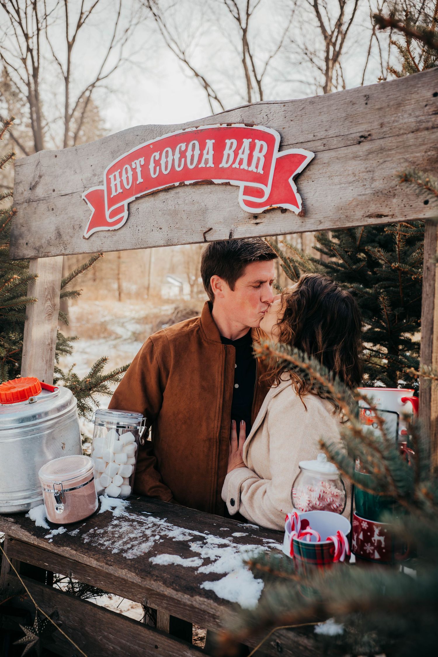 A rustic hot cocoa bar setup with vintage containers and festive winter decorations in an outdoor setting.