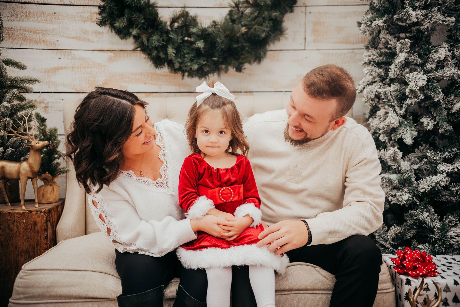 A family poses together in front of a festive Christmas scene with wreaths and decorated trees.