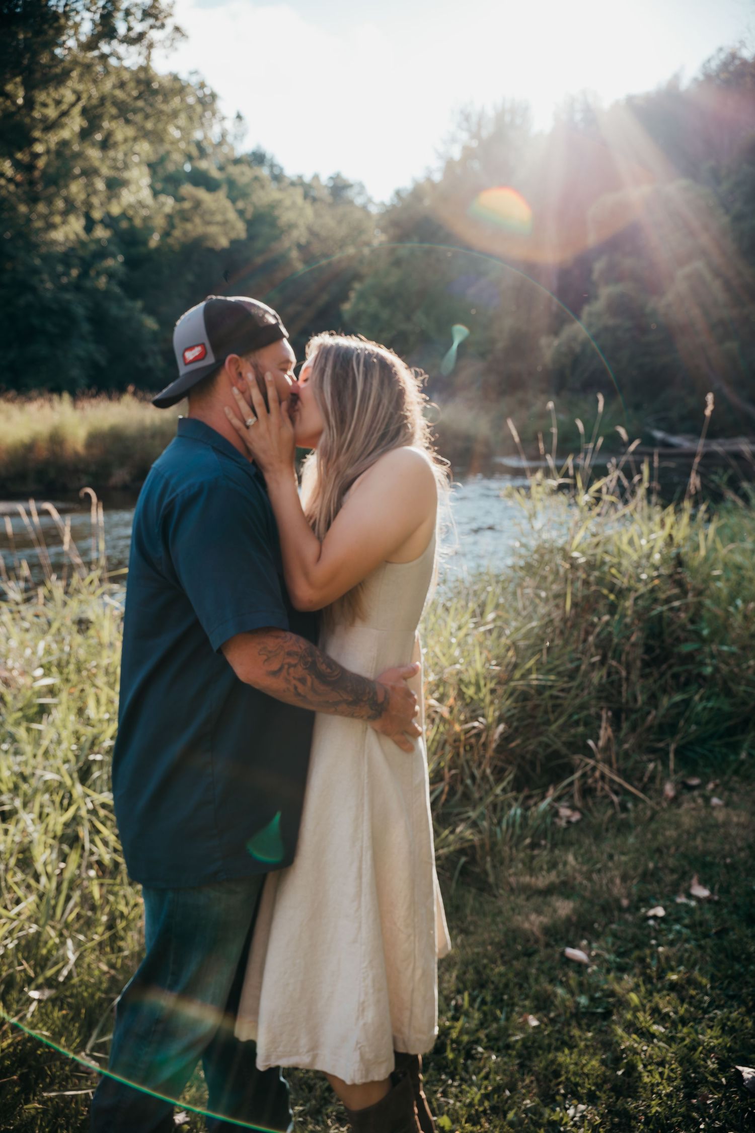 A couple shares a romantic kiss in a sunlit meadow during a golden hour photoshoot.