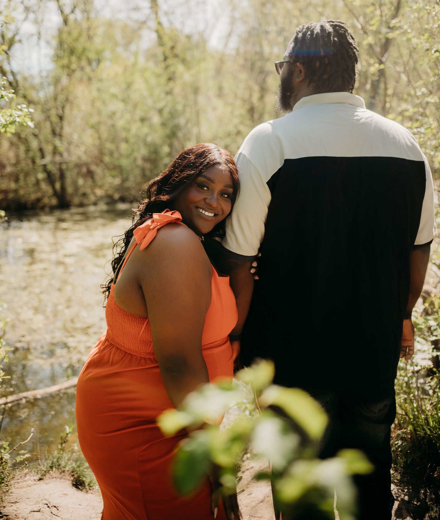 A couple shares a romantic moment in nature, with the person in orange leaning against their partner in a candid shot.