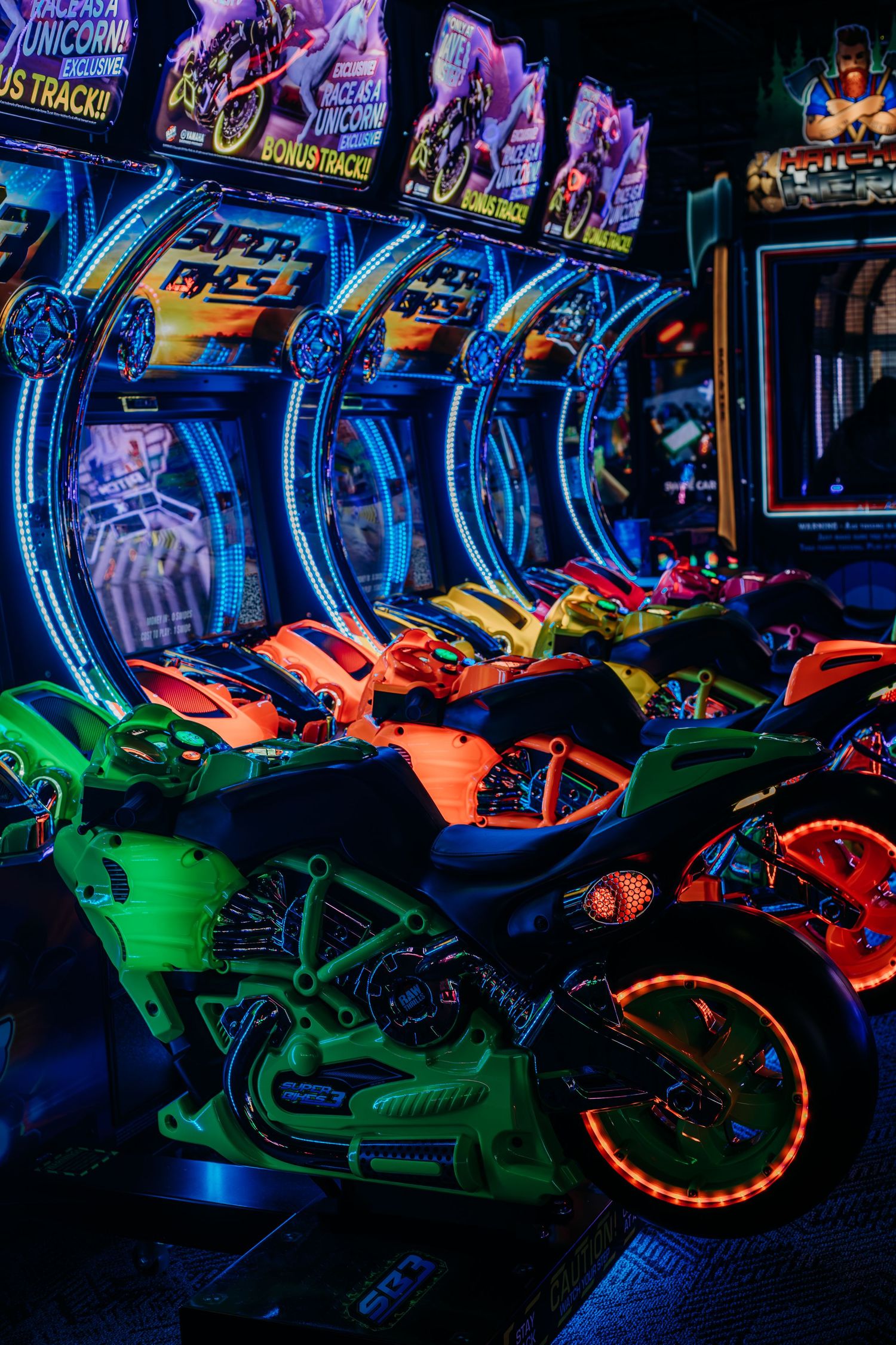 Colorful neon-lit motorcycles on display at an arcade with vibrant blue and green lighting effects.