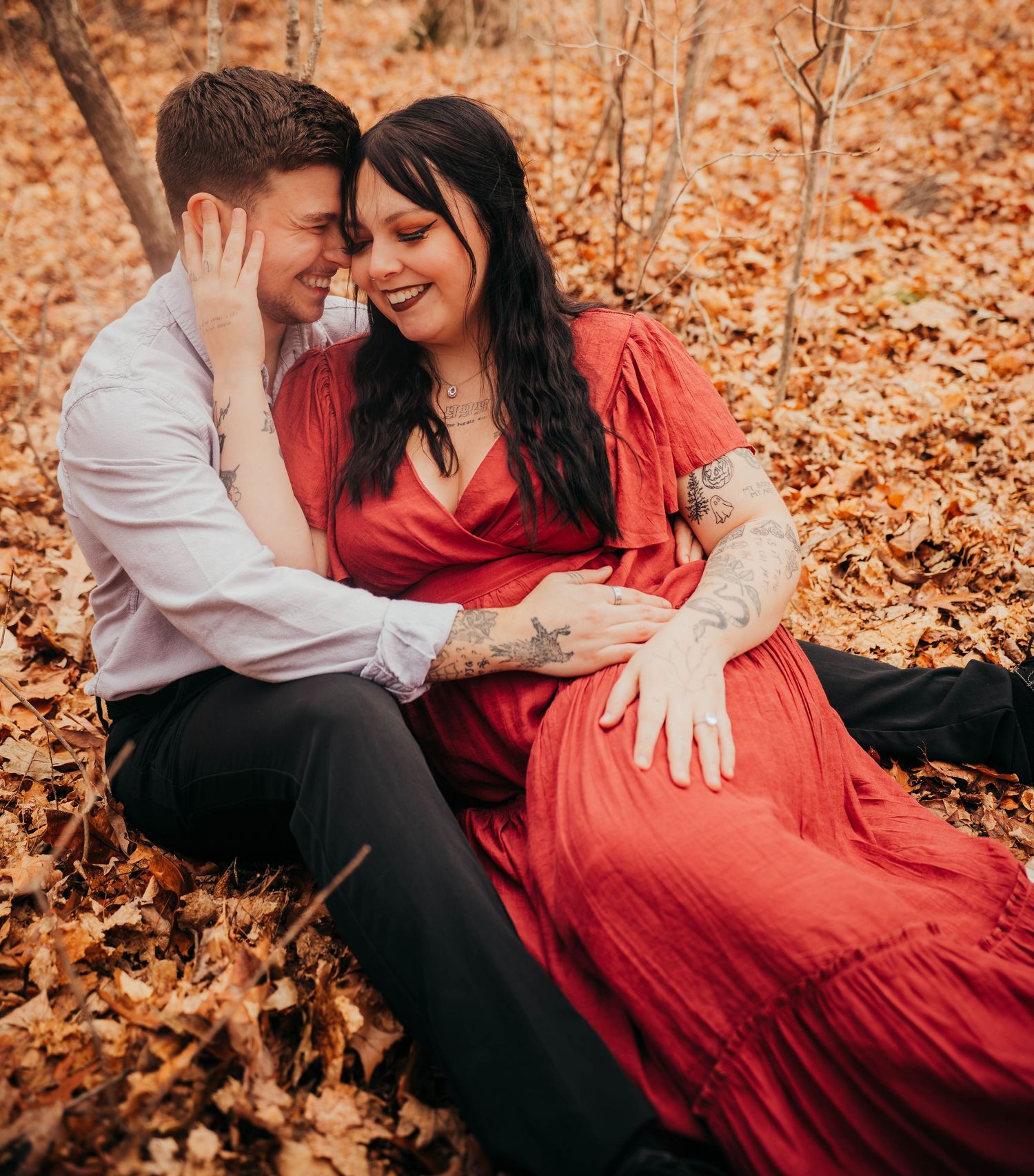 A couple shares an intimate moment while sitting among fallen autumn leaves in a romantic outdoor setting.