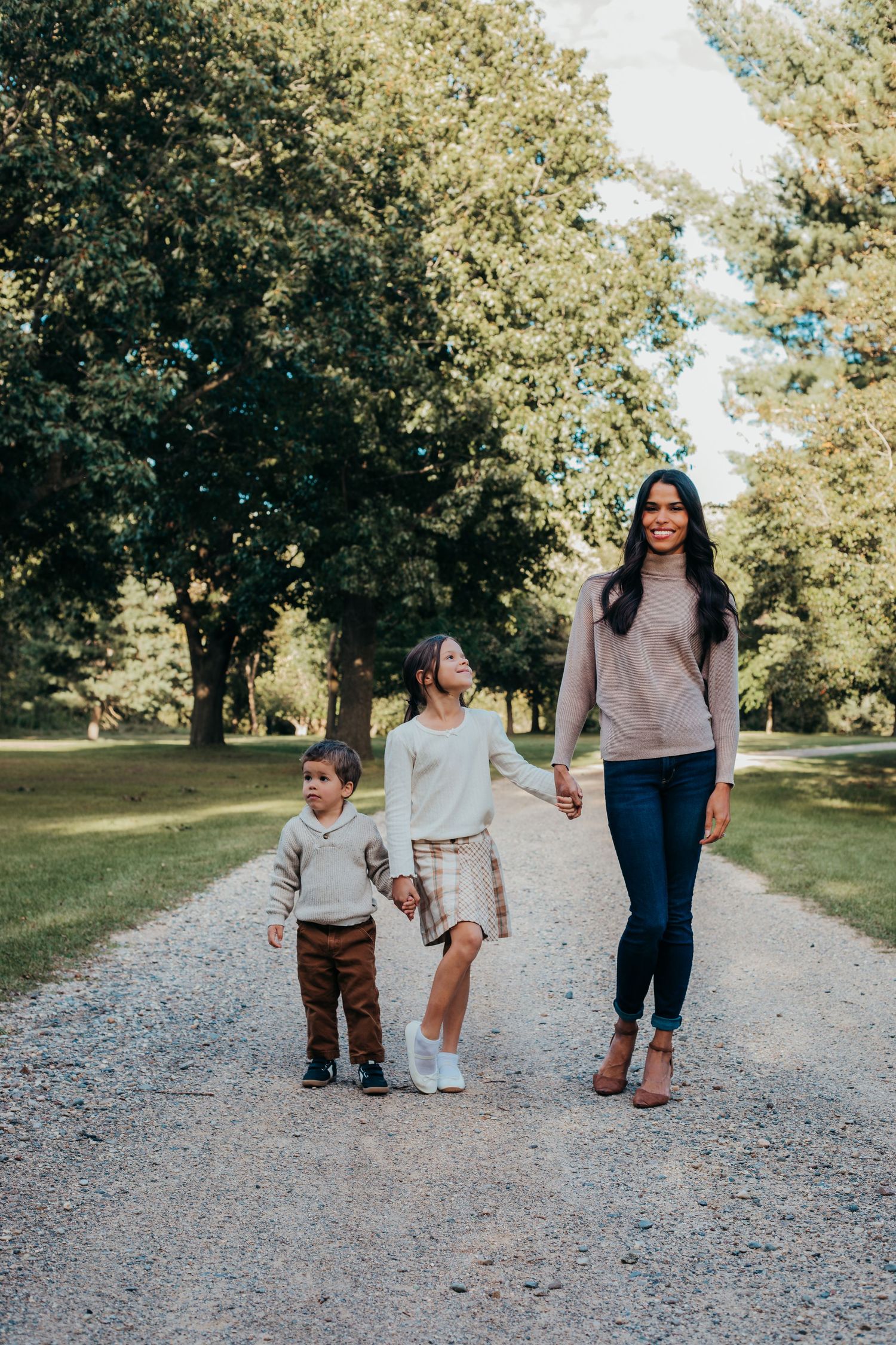 Children and adult walking together on a gravel path through a park on a sunny autumn day.