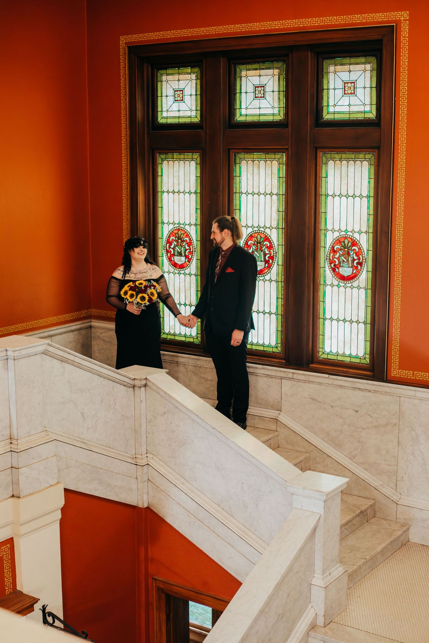 Elegant staircase with stained glass windows and white marble steps in a historic building with orange walls.