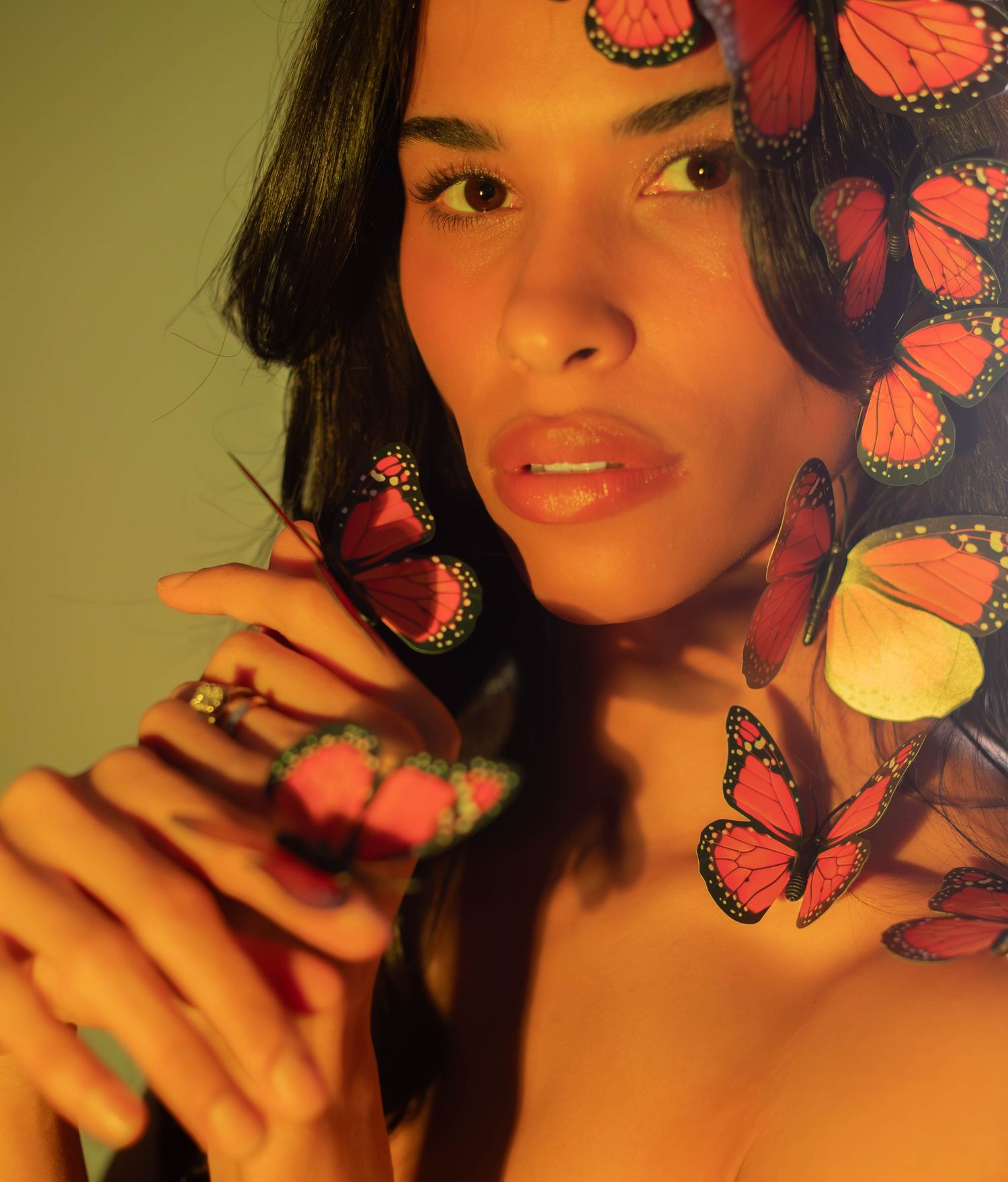 Artistic portrait with vibrant monarch butterflies surrounding the subject in warm lighting against a dark background.