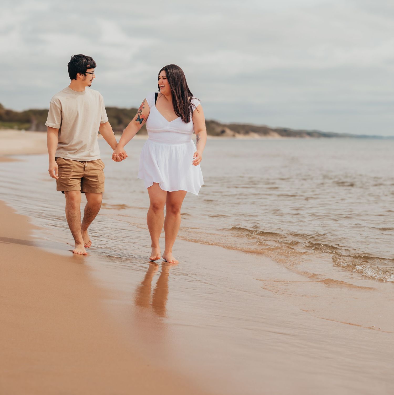 Couple walking hand in hand along the shoreline at sunset with waves gently lapping at their feet.