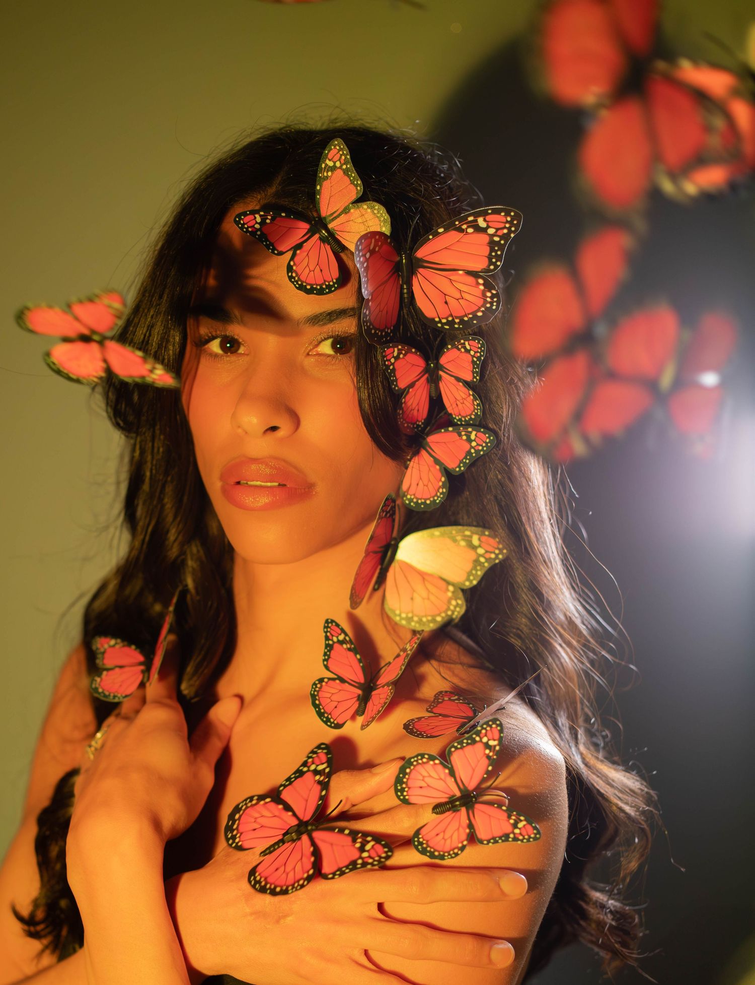 Artistic portrait with orange monarch butterflies creating a dreamy effect against a dark background.
