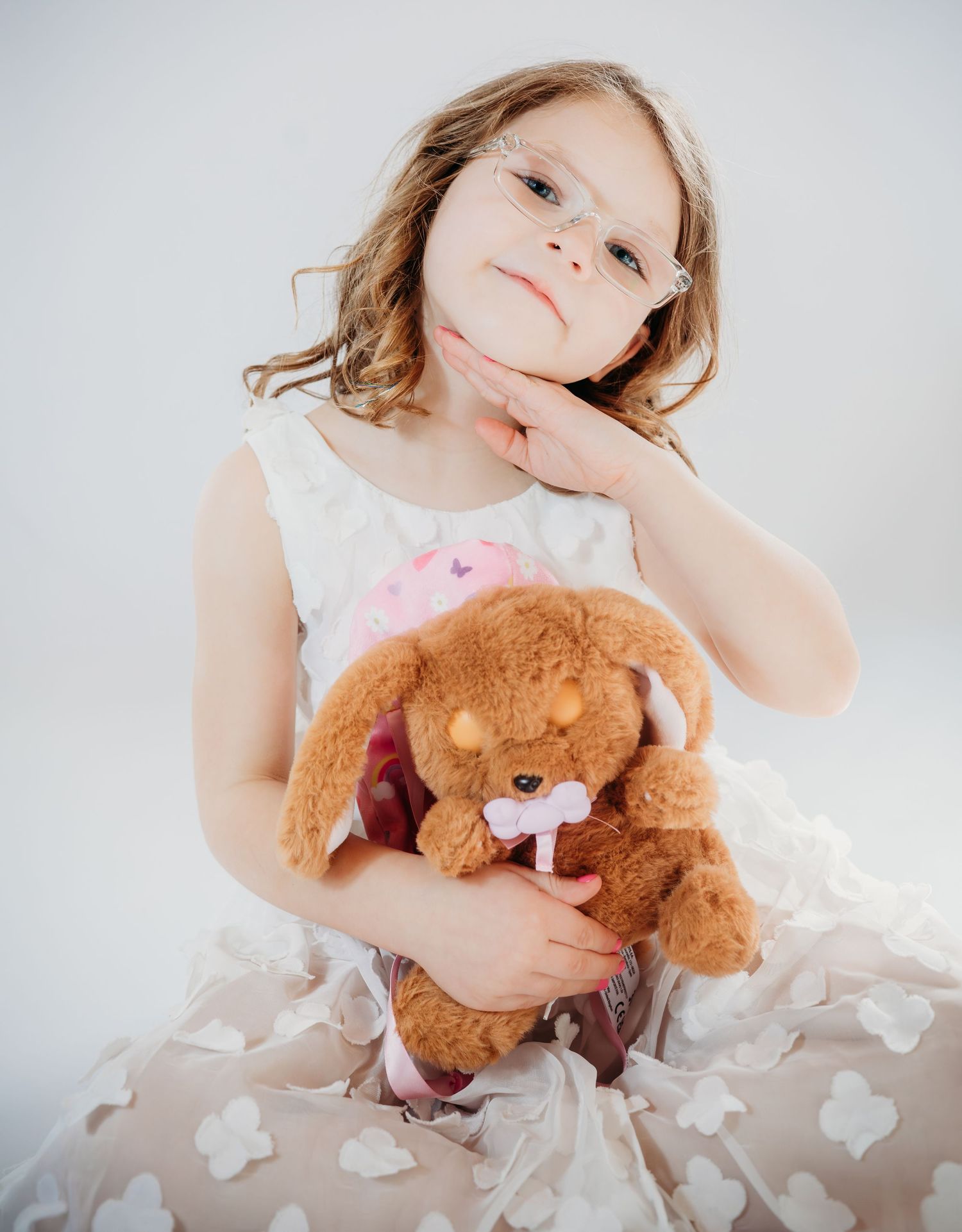 A series of four photos showing a child in a white dress holding and cuddling with a brown teddy bear.