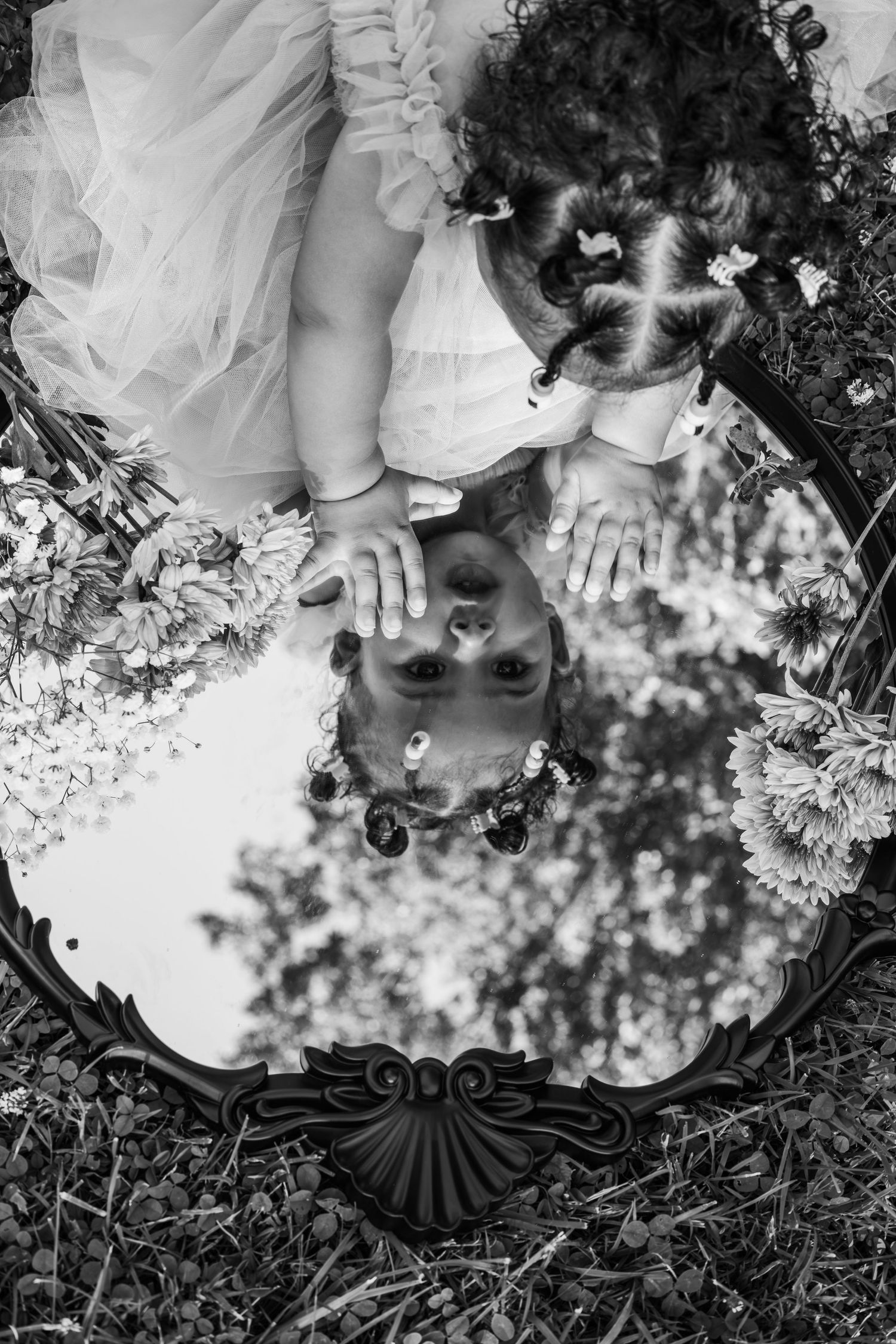 Black and white overhead view of small feet in grass surrounded by delicate white daisies and flowers.