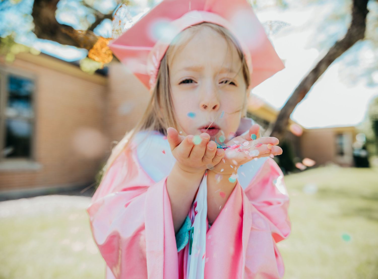A child wearing a pink raincoat and hat plays outdoors in a series of candid moments on a sunny day.