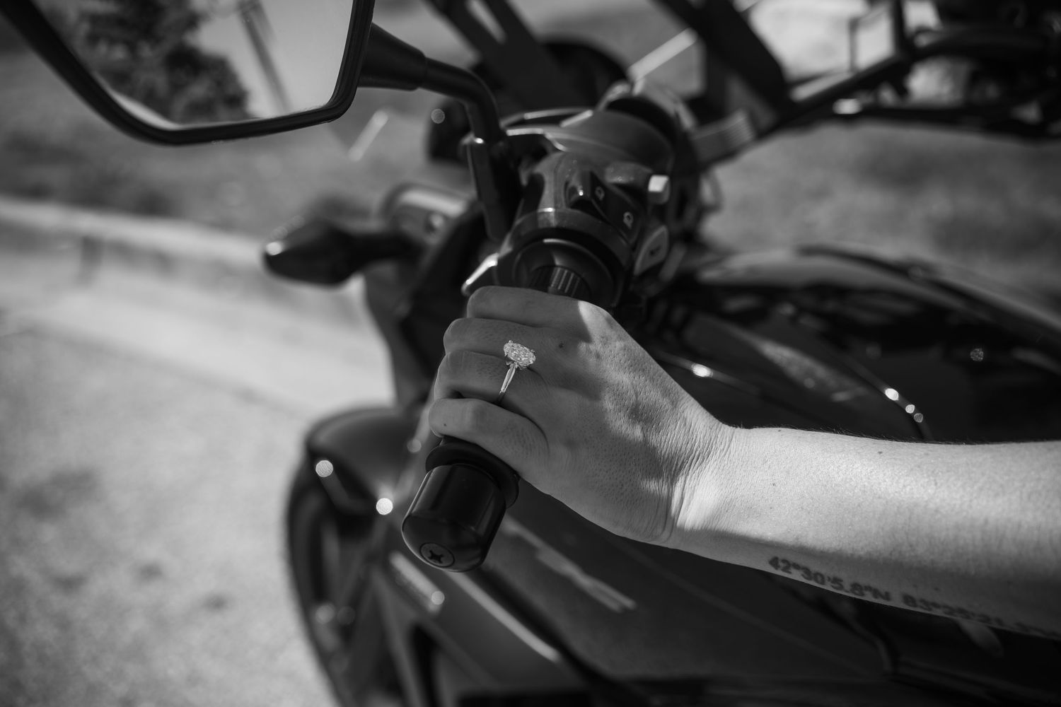 Close-up view of a black motorcycle handlebar with brake lever and controls against a blurred background.