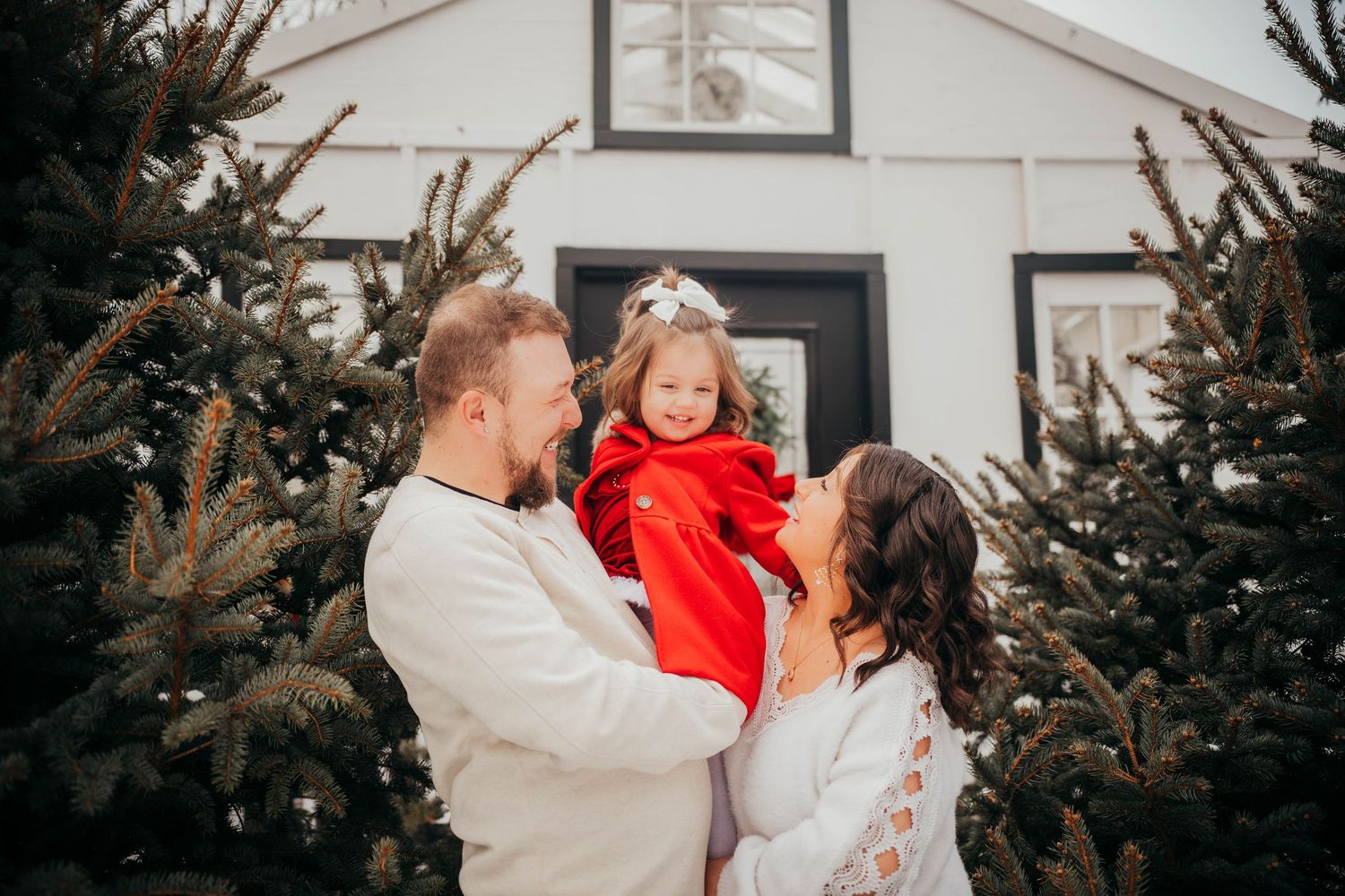 A loving family shares joyful moments together while standing among evergreen Christmas trees outdoors.