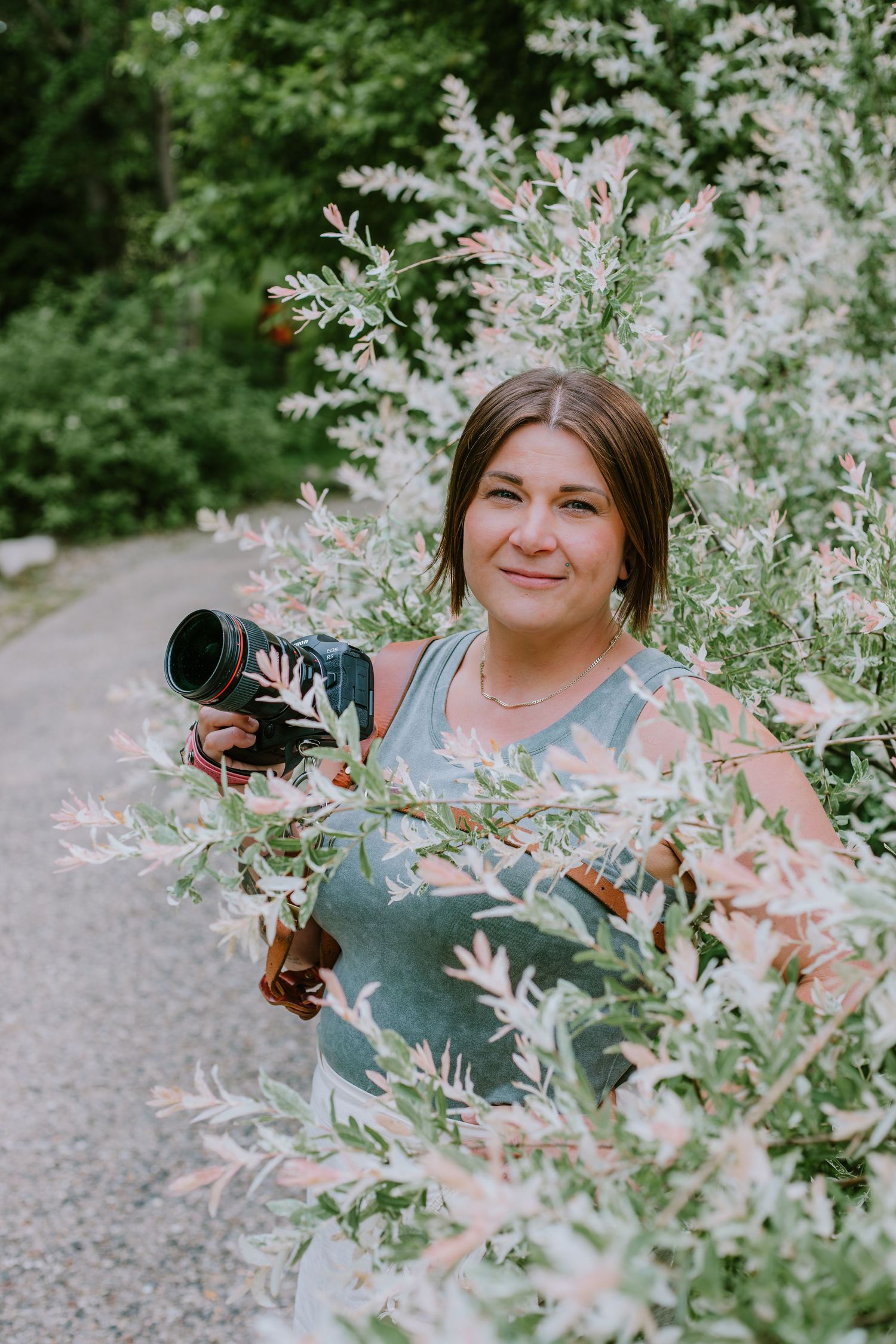 A photographer poses among blooming white astilbe flowers in a garden setting.