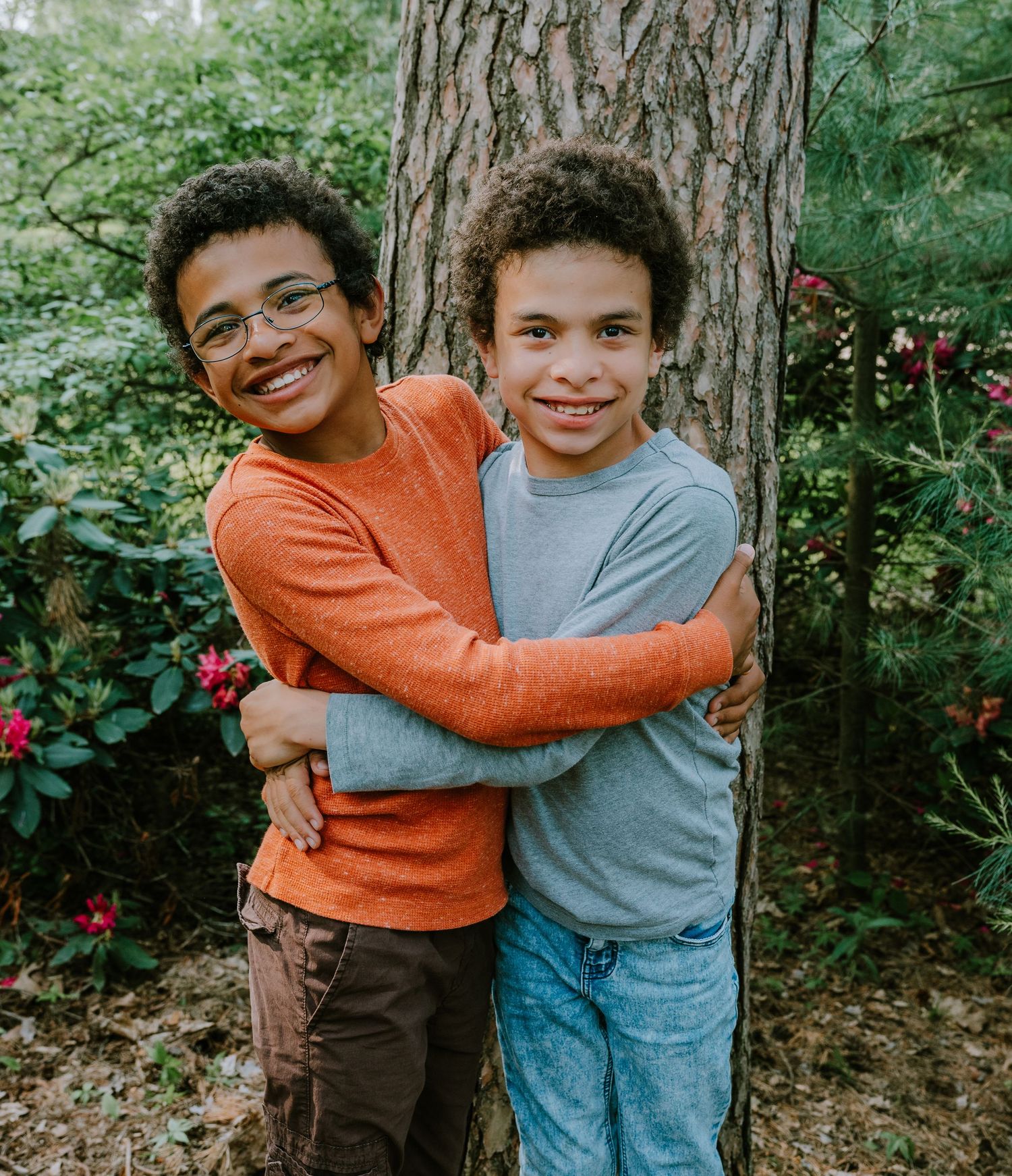 Two people sharing a warm embrace outdoors among trees and flowering bushes.